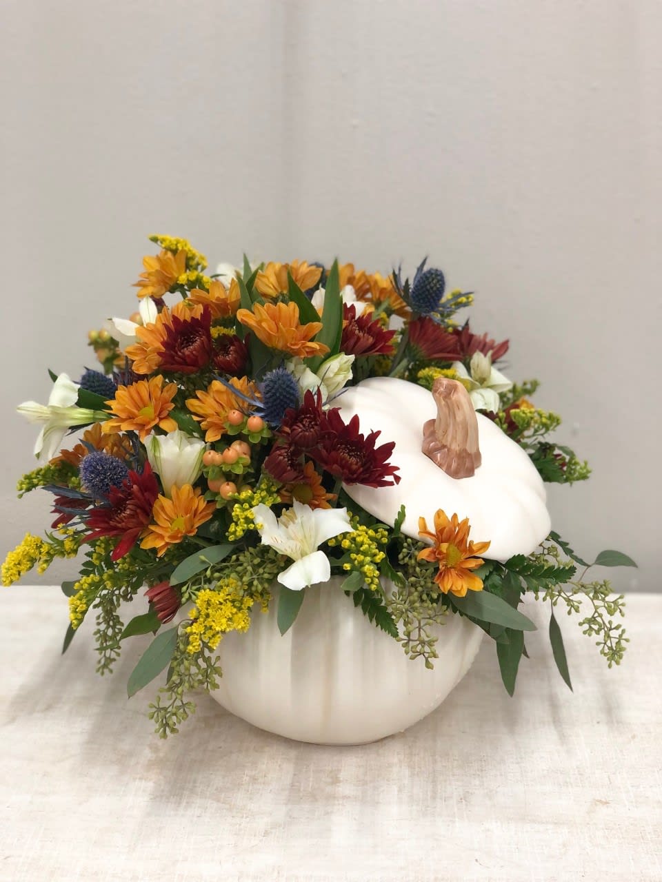 Candied Pumpkin Bouquet - Bright fall colors really pop inside this beautiful white ceramic pumpkin, perfect for the season! This lovely keepsake can be used during your dinner table at Thanksgiving or to hold some real candy!  Flowers and colors may vary depending on availability.