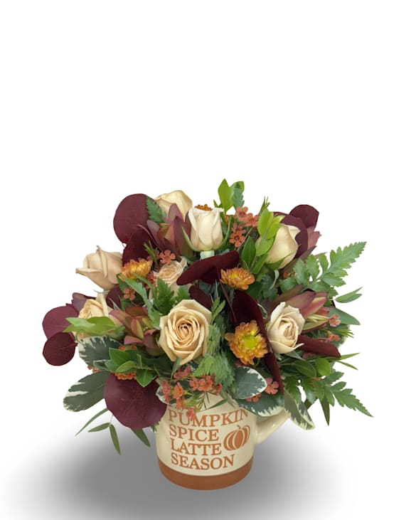 Latte Season - Celebrate cozy autumn vibes with this charming arrangement in a seasonal mug featuring either “Pumpkin Spice Latte Season” or “Pumpkin Spice and Everything Nice.” Filled with tan spray roses, orange wax flowers, warm-toned pom poms, safari, and tinted eucalyptus, it measures approximately 8.5” x 5” and is perfect for brightening a desk, kitchen, or cozy corner.