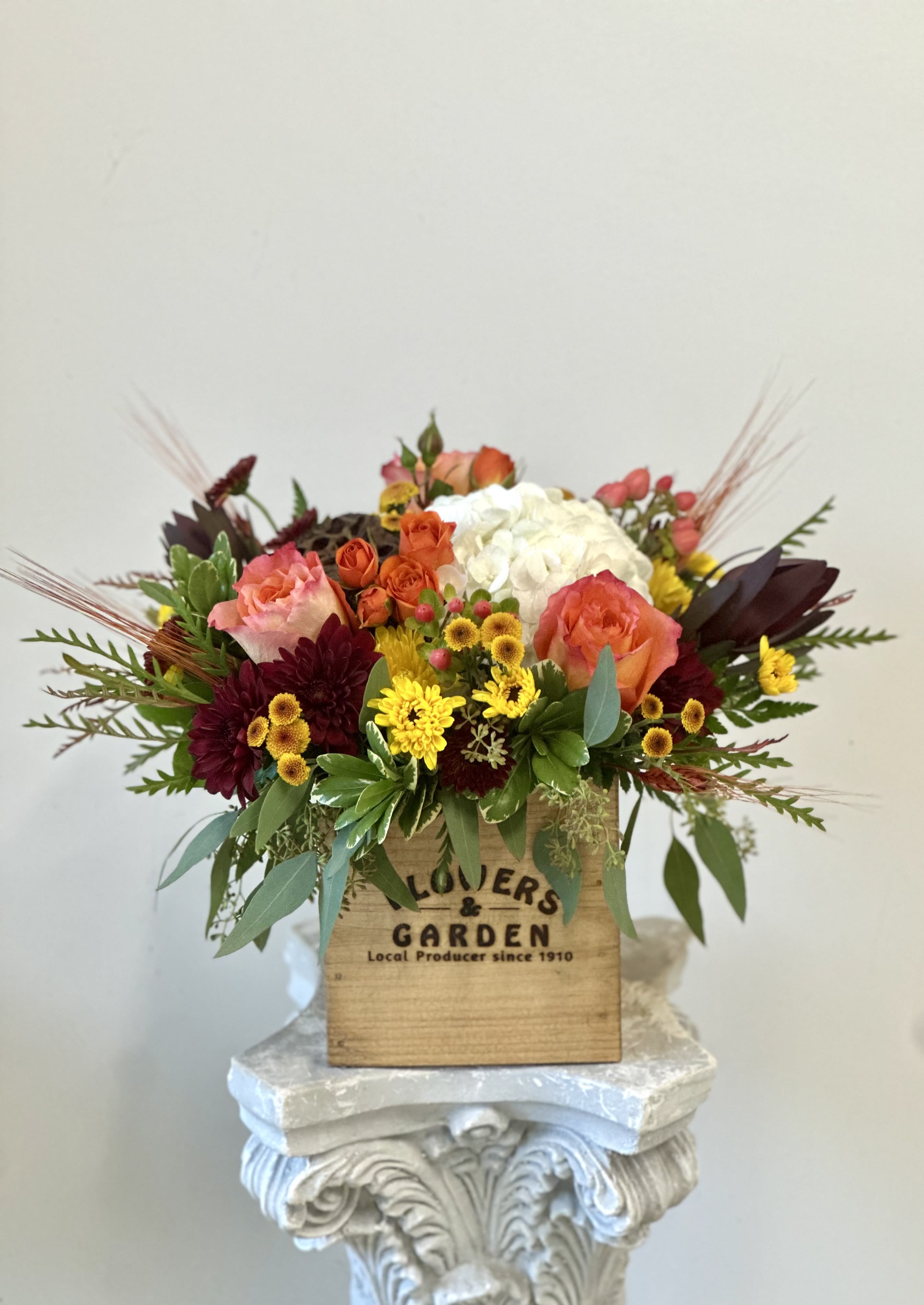 Autumn Sunset by Westford  Florist - Embrace the warm embrace of fall with the exquisite Autumn Sunset arrangement by Westford Florist. This captivating bouquet features vibrant orange roses and delicate spray roses, harmoniously blended with bountiful white hydrangeas and rich hypericum berries. The addition of safari sunset blooms, burgundy and yellow poms, along with charming dry pods and seasonal greenery, creates a stunning tableau that captures the essence of autumn. Nestled artfully in a rustic wooden box, this arrangement not only brightens any space but also serves as a stylish focal point that brings the colors of the season indoors. Perfect for gifting or elevating your own decor, Autumn Sunset is an elegant celebration of nature’s beauty during this enchanting time of year. Experience the splendor and warmth of autumn today.