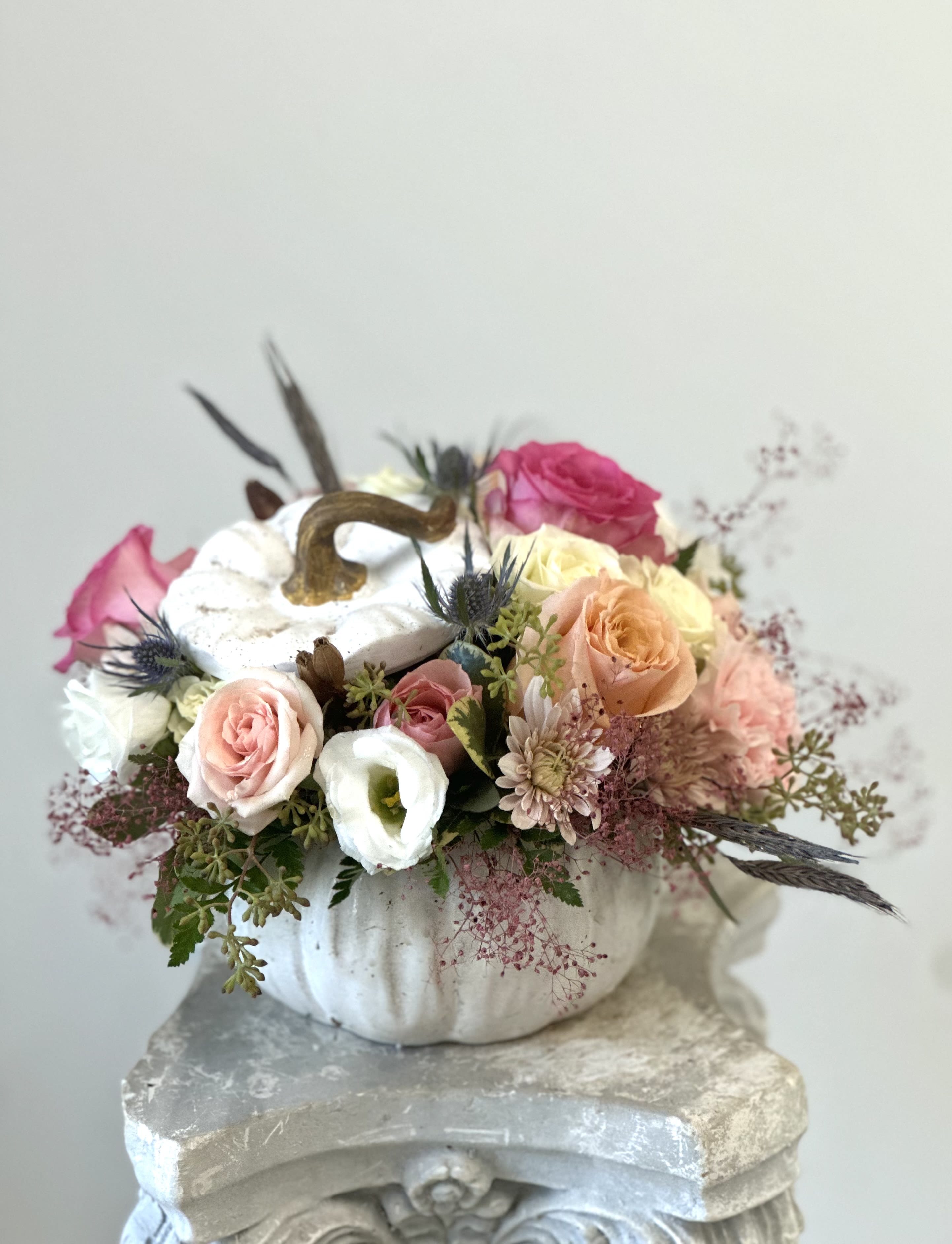 White Pumpkin Delight - Transform your space with the exquisite White Pumpkin Delight, a stunning arrangement that embodies elegance and charm. This unique centerpiece features an enchanting selection of pristine peach and pink roses, delicate peach spray roses, soft peach poms, blue thistle—all artfully nestled within a chic white pumpkin. The cut-off top adds a whimsical touch while allowing for easy access to admire the blooms from every angle. Perfect for home decoration or as a captivating focal point at gatherings, this delightful composition is designed to elevate any occasion. Let the serene palette of whites and peaches infuse your environment with warmth and sophistication. Elevate your decor today with this one-of-a-kind masterpiece that promises to leave a lasting impression on all who encounter it.