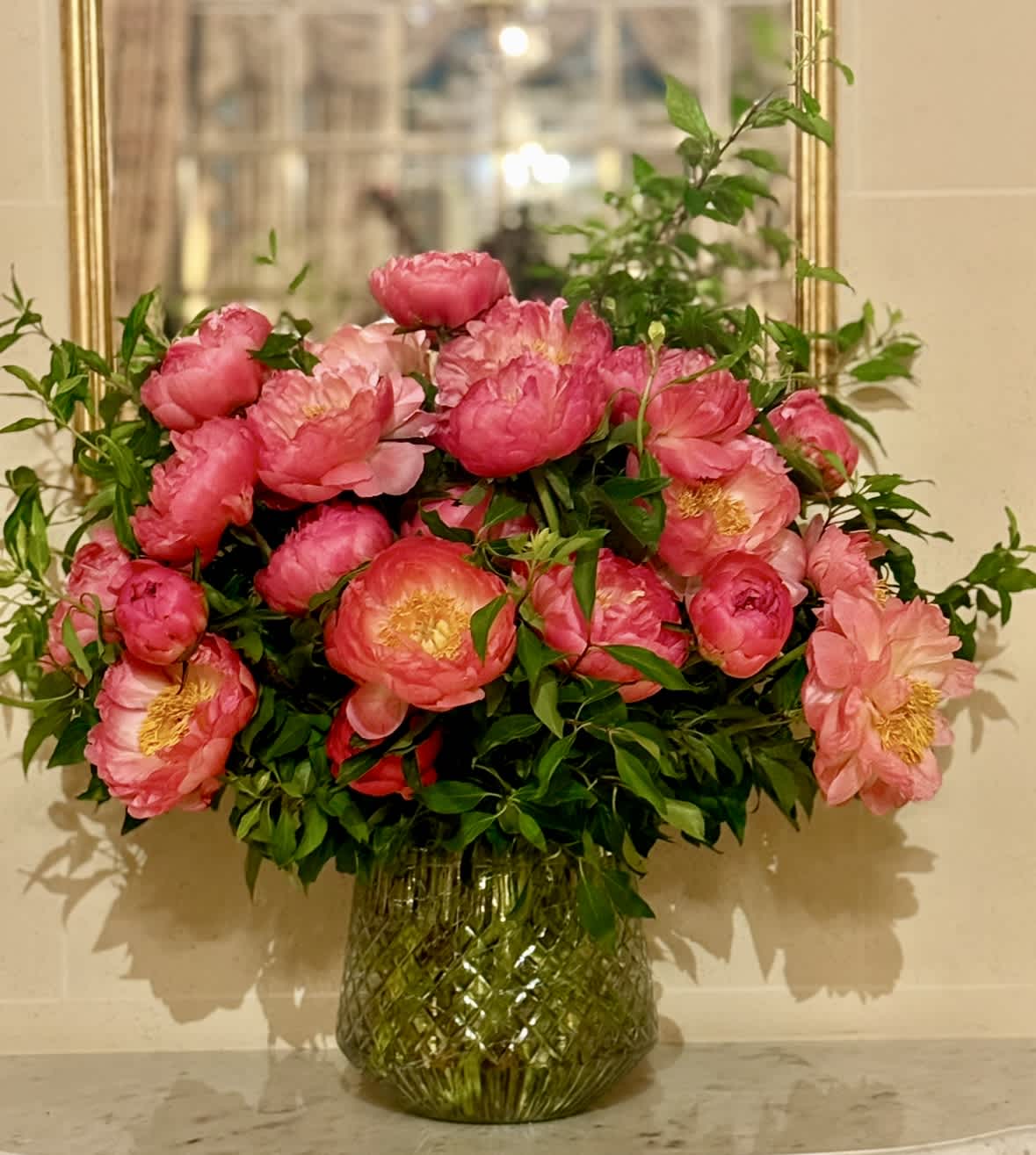 PEONY MAGIC - A beautiful display of a 18 peonies designed with flowering branches and Italian ruscus in a beautiful 8 x 8 gold container.
