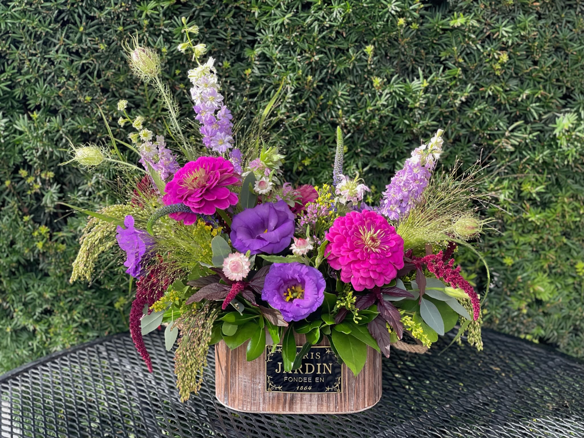 Parisian Prairie - Transport yourself to the French countryside with our Parisian Prairie floral arrangement. This textural assortment evokes an explosion of wildflowers with a mix of fresh blooms, including purple lisianthus, fuscia zinnias, larkspur, burgundy amaranthus, and dynamic grasses, presented in a rustic wooden French garden box.
