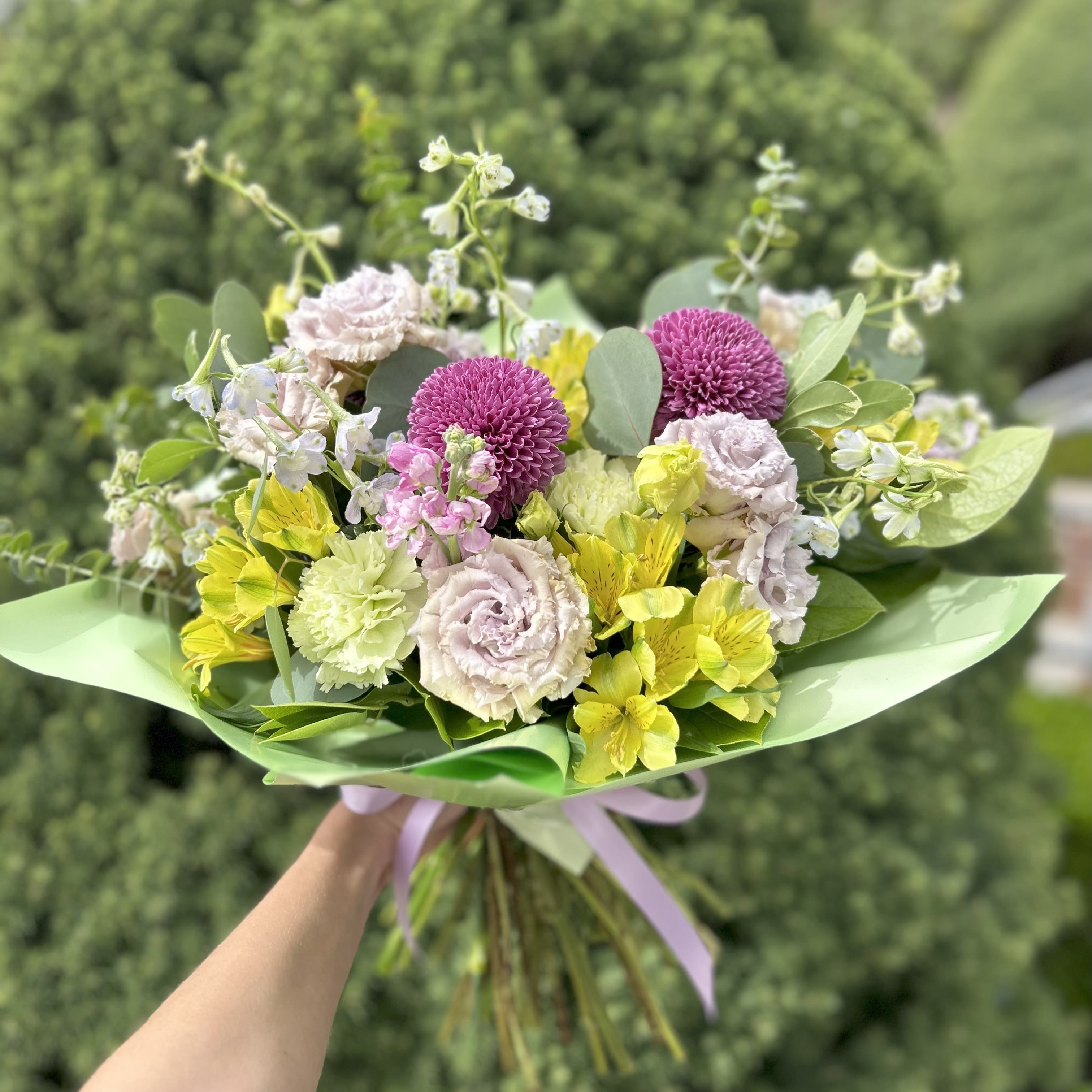 Lavendar Lisi - A sweet juicy bouquet of lavender lisianthus, yellow alstroemeria, light blue delphinium, and adorable green carnations, wrapped in decorative paper and tied in a bow. This is the perfect gift for your niece's dance recital or birthday. 