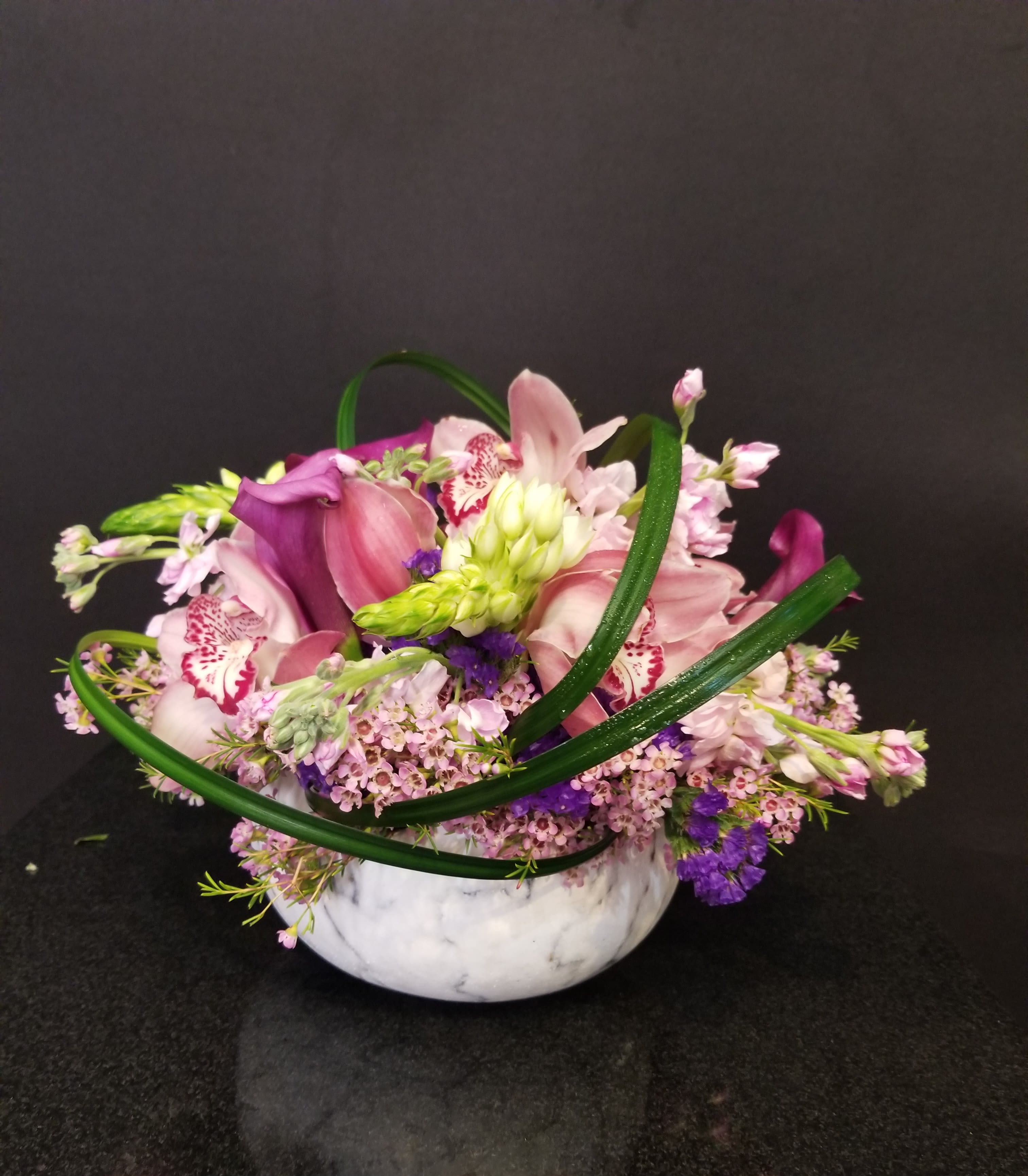 Enchanted Garden - A graceful blend of orchids, calla lilies and delicate seasonal blooms arranged in a chic bowl. Accented with fresh greenery and soft lavendar tones, this design is both modern and romantic. Perfect as a centerpiece or a thoughtful gift. 