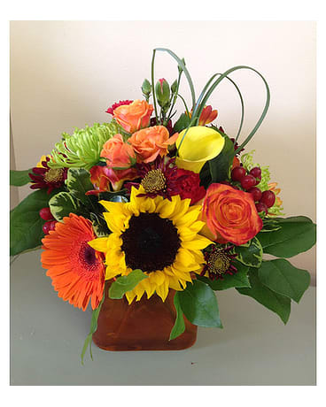 Orange Sunset - Sunflowers gerbera daisies circus roses calla lilies mums daisies spray roses mini carns hypericum berries all arranged together in an orange vase. All flowers and colors are subject to change due to availability.   FCF-510