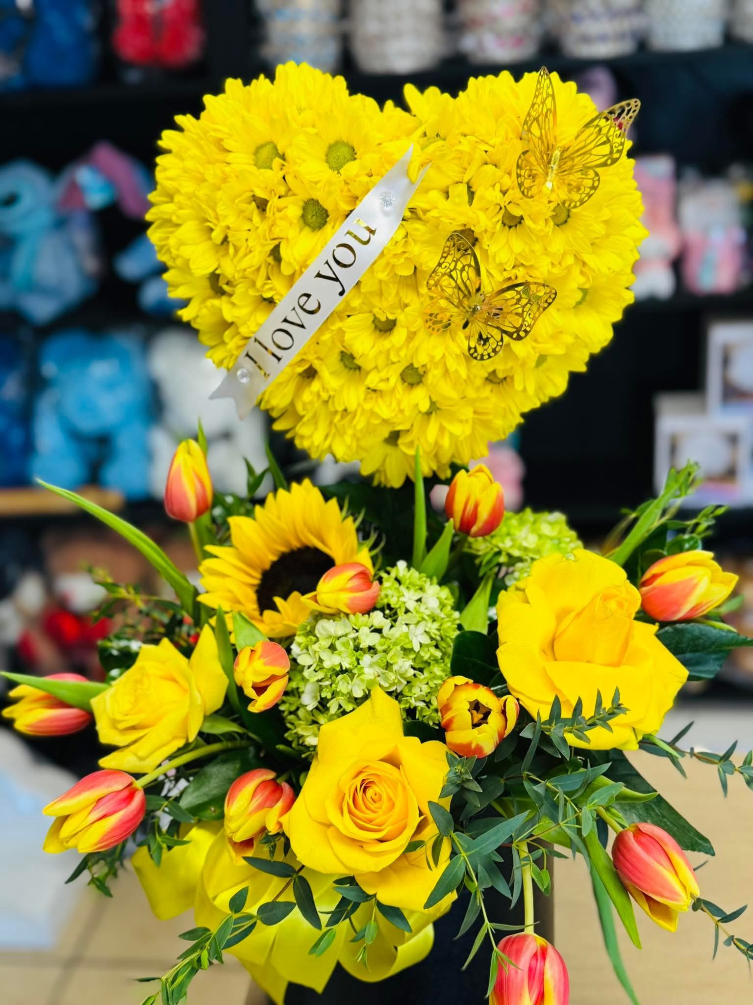 Yellow heart floral arrangement - Beautiful floral arrangement in the shape of a heart, consisting of yellow Daisies, yellow roses, sunflowers, and tulips (only in tulips season) (you can customize the ribbon or card with short message) available every day.