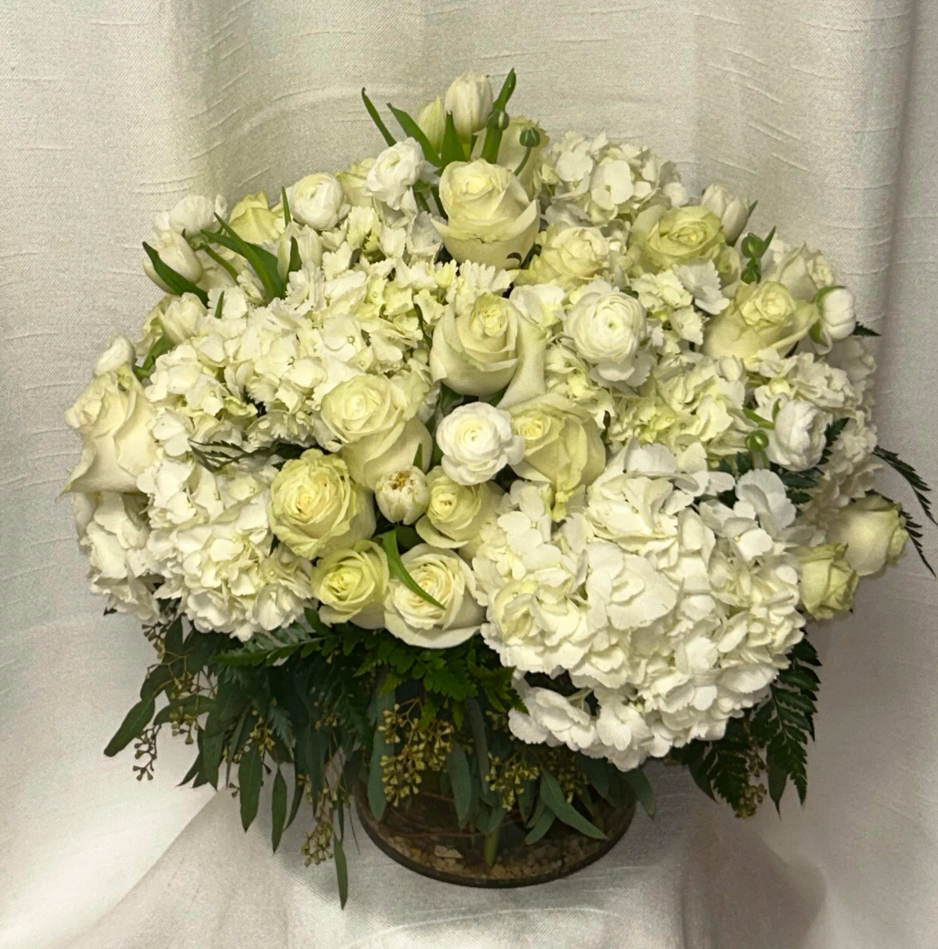 Vanilla Sky (DB) - Experience the epitome of modern elegance with our stunning Vanilla sky floral arrangement featuring white hydrangea, creamy white roses, and white tulips, arranged in a leaf-lined cylinder vase. This contemporary display is the perfect blend of sophistication, grace, and minimalism.    