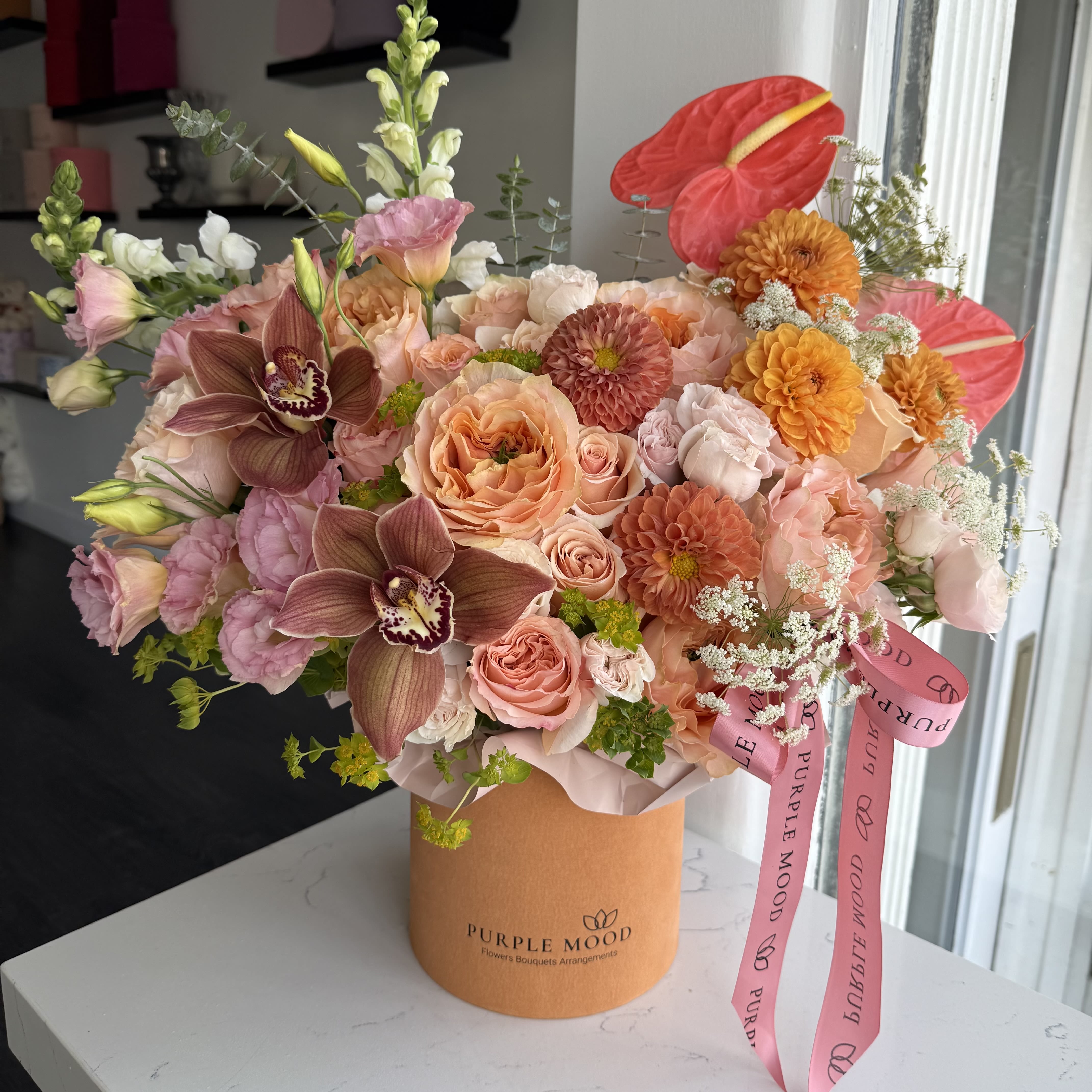 Golden Hour Box - Standard container size - D6.75'x H7.5'  Deluxe container size - D8.25'x H9.5'  Our Golden Hour Box captures the magic of a glowing sunset with its radiant mix of warm tones and striking textures. This vibrant arrangement feels joyful, luxurious, and full of energy — a perfect centerpiece for celebrations or a heartfelt gift that makes a lasting impression.      •    Warm, golden and peachy hues with bold accents     •    Designed in a signature hatbox for modern elegance     •    Radiant, eye-catching, and full of character
