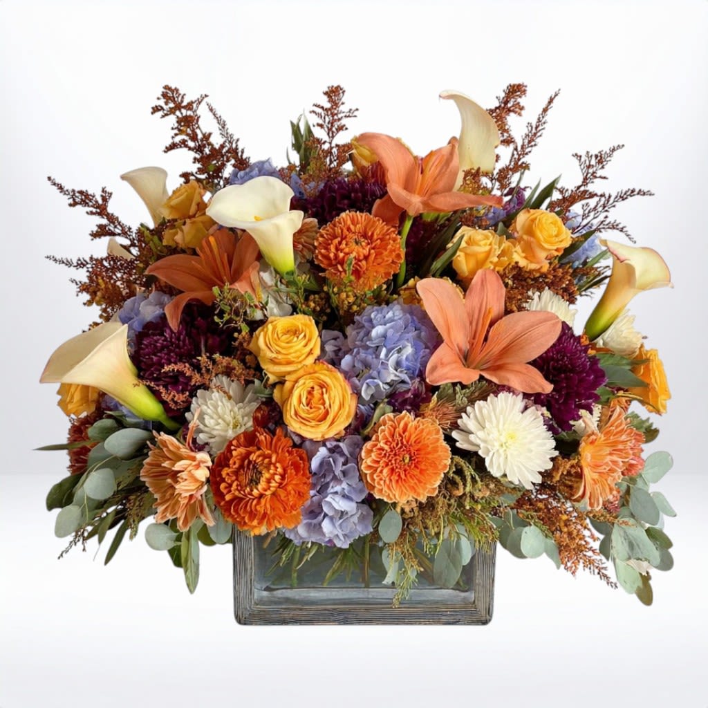 Autumn Splendor Centerpiece - The Autumn Splendor Centerpiece is a grand celebration of fall’s most vibrant blooms. Designed in a rustic wooden container, this arrangement features golden yellow roses, rich orange lilies, creamy calla lilies, soft blue hydrangea, and seasonal mums in shades of orange, burgundy, and ivory. Accented with textured foliage and autumn fillers, it’s an abundant design that captures the warmth and richness of the season.  Perfect for Thanksgiving gatherings, fall birthdays, or as a striking centerpiece, this bouquet brings festive elegance to any table. Available for same-day flower delivery in Galveston, Houston, and surrounding areas.  Substitution Disclaimer: Due to seasonal availability, some blooms may be replaced with similar varieties of equal or greater value to maintain the design’s look and integrity. Your arrangement will always reflect the same spirit, palette, and premium quality.