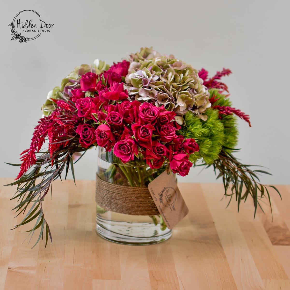 Ring of Fire -   The &quot;Ring of Fire&quot; arrangement bursts with bold and passionate hot pink spray roses, their vibrant hues commanding attention and exuding energy. The lush hydrangeas contribute to the flower arrangement's depth and visual appeal. At the same time, the elegant dianthus adds a touch of delicate beauty. The seasonal greens provide a refreshing contrast, lending the composition a natural and organic feel.  Housed in a clear, rustic glass container adorned with jute rope, the &quot;Ring of Fire&quot; arrangement exudes a rustic charm that complements its vibrant and dynamic nature. Combining the rustic container and the elegant blooms creates a unique separation, enhancing the overall appeal of the bouquet.  Whether it's a centerpiece for a special event, a romantic gift, or a vibrant addition to any space, the &quot;Ring of Fire&quot; floral arrangement will leave a lasting impression. Its bold pop of color, visually appealing design, and diverse selection of blooms make it a perfect choice to bring a touch of unique beauty to any occasion.  At Hidden Door Floral Studio, we commit to crafting extraordinary floral arrangements that captivate the senses. With our same-day florist delivery services available in Cary, Duram, Raleigh, Morrisville, Apex,  and Wake Forest, you can trust that your &quot;Ring of Fire&quot; arrangement will arrive fresh and vibrant, ready to illuminate the atmosphere and create a memorable experience.