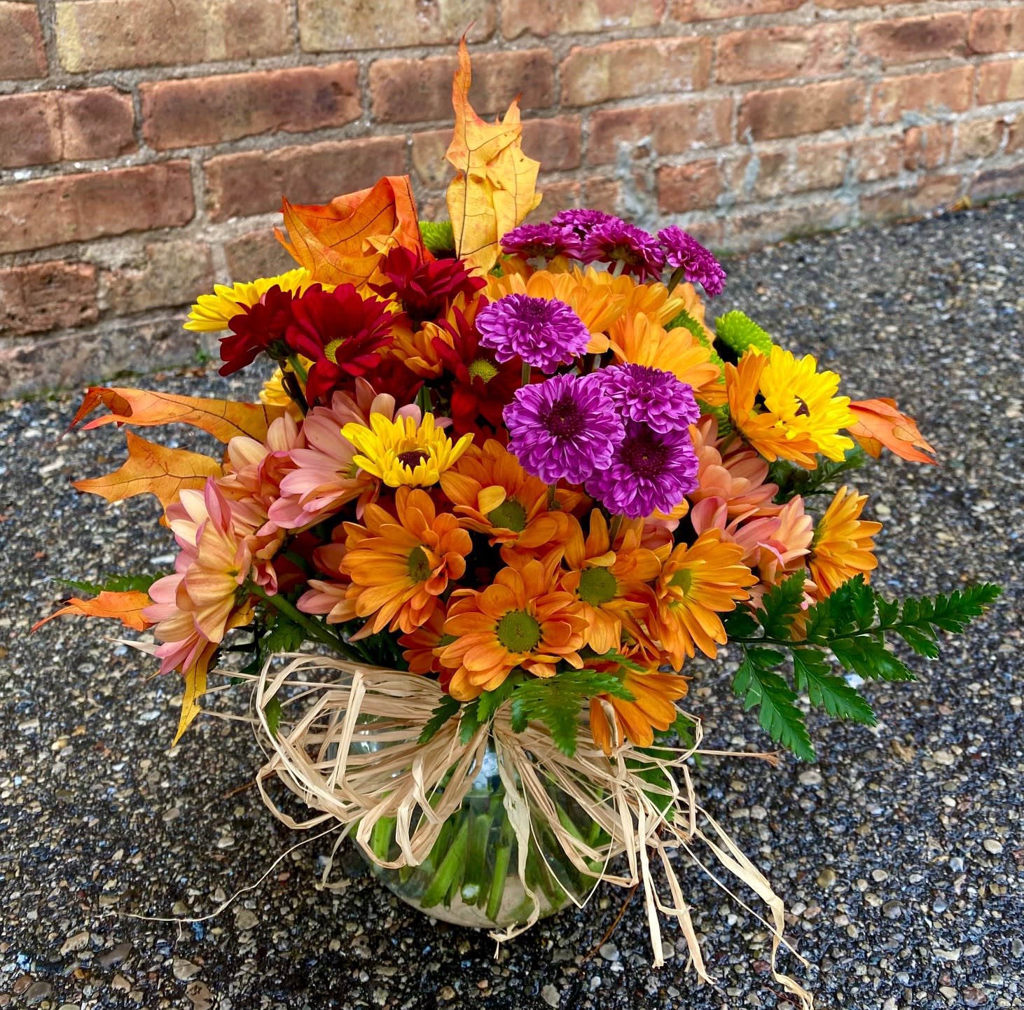 Fall Sunshine - The warm colors of fall sunshine are featured in this beautiful arrangement. A touch of fall leaves and a raffia bow compliment the mixed fall mums in a glass bowl. Perfect for any occasion. If you choose Deluxe the arrangement will be larger and fuller. Vase shape may vary.  We are proud to deliver our flower creations to the Kenosha, Somers, Bristol and Pleasant Prairie area. With over 55 years of combined flower design experience in Kenosha, Wisconsin, A Summer's Garden Florist and Gifts is the perfect choice for the freshest flowers, most creative design and exceptional customer service.