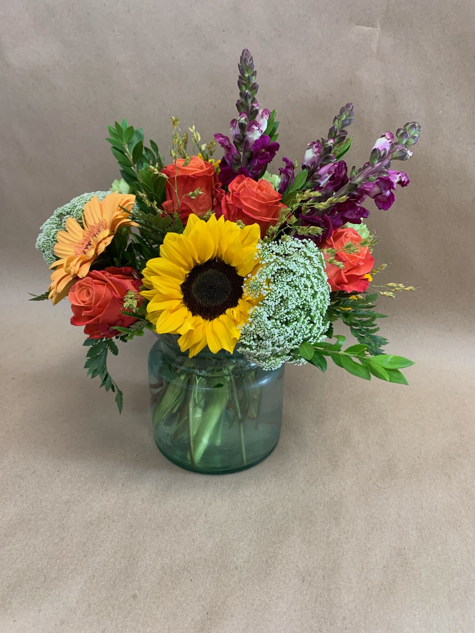 Fall Fantasy - Bring the beauty of autumn indoors with this vibrant arrangement. Featuring cheerful sunflowers, bold orange roses, and rich snapdragons. Designed in a glass vase, it’s perfect for brightening up any table or sending a heartfelt gift that captures the warmth and color of fall.  This bouquet is bursting with seasonal charm.