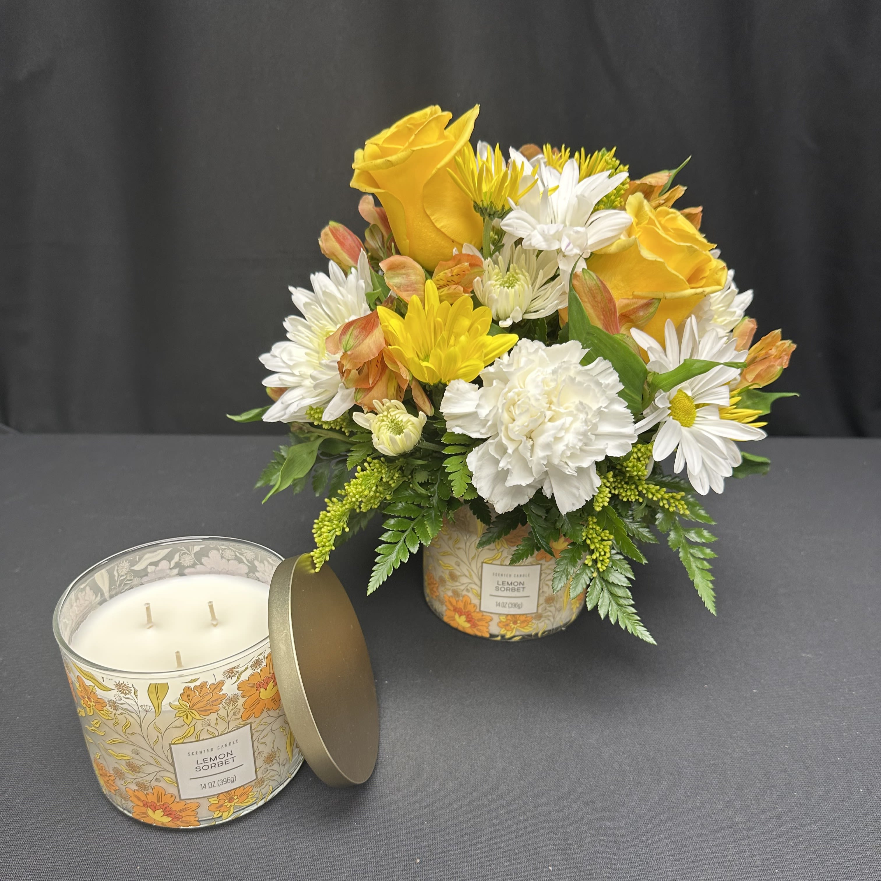 Sunlit Glow - Brighten any space with this radiant pairing of fresh blooms and a fragrant candle. Golden yellow roses, cheerful daisies, and crisp white carnations are artfully arranged atop the lid of a lemon sorbet candle, creating a gift that delights the senses. Perfect for birthdays, thank-yous, or just because, Sunlit Glow brings warmth, cheer, and a touch of sunshine to every occasion.