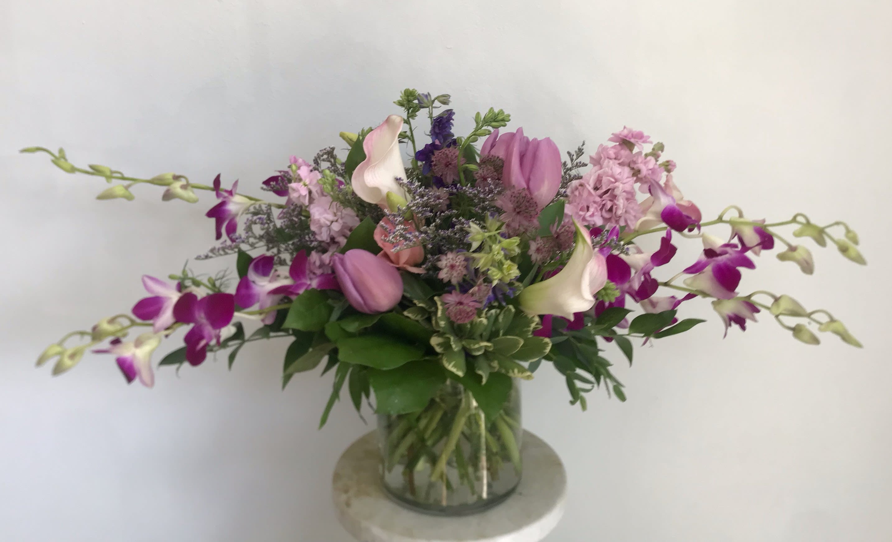 Elegance Elegance - Purple and pink toned flowers arranged in The Twisted Tulip's Euopean signature style. This arrangement is perfect for the unique and classy. Pictured are Calla Lilies, Dendrobium Orchids, Tulips, and Snap Dragons and other beautiful flowers. Your arrangement will be designed in the style shown but flowers and containers may be different from that pictured.