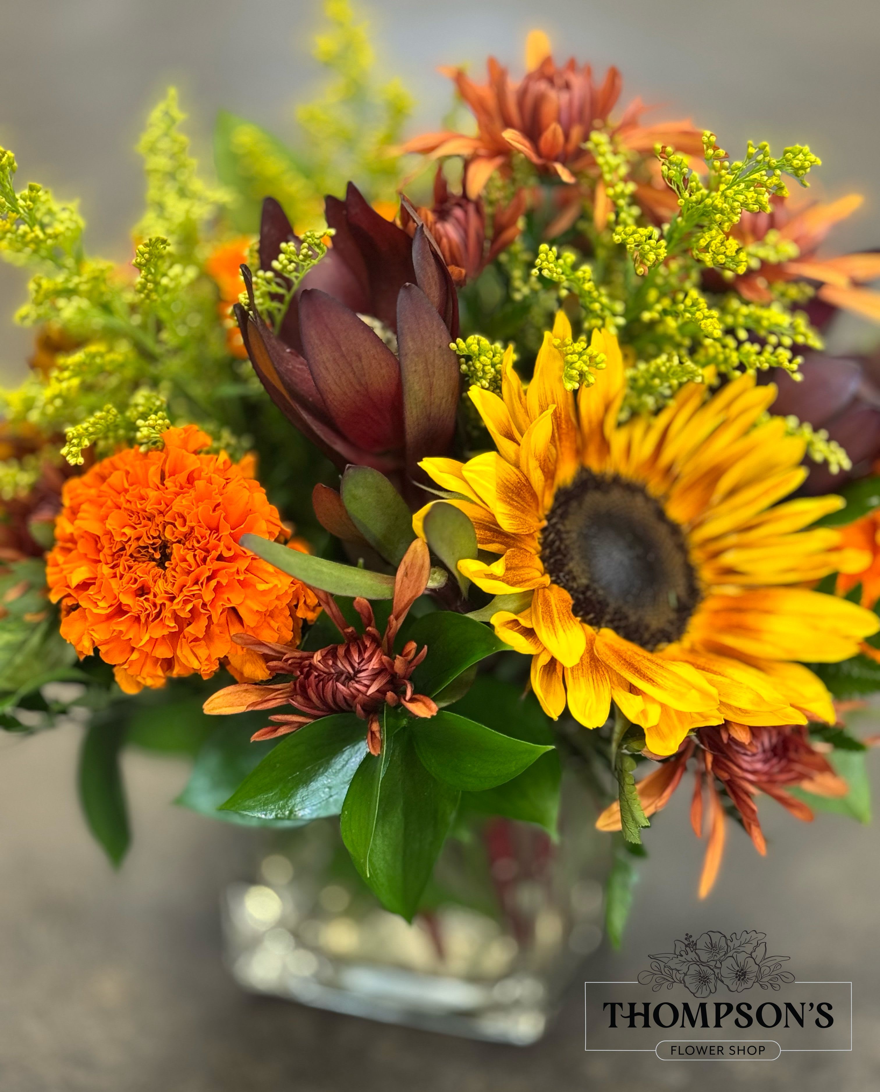 Marigold Meadows - Celebrate the colors of fall with this vibrant design featuring bold sunflowers, glowing marigolds, bronze chrysanthemums, and seasonal textures. Arranged in a modern glass vase, this cheerful bouquet brings the golden warmth of autumn right to the table. Perfect for birthdays, seasonal celebrations, or as a thoughtful pick-me-up, this arrangement captures the beauty of Arizona’s fall sunsets in every bloom. 