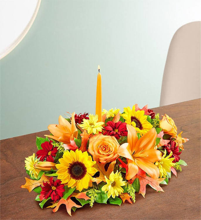 Fall Centerpiece - Roses. Sunflowers lilies arranged im a long low style. Orange candle in the middle. Fall leaves