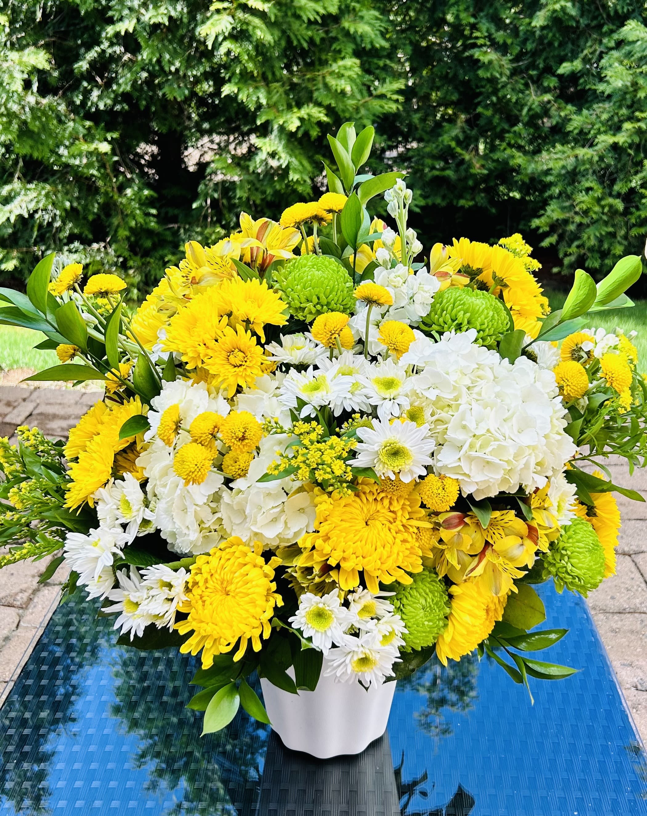 Sweetness Arrangement - This arrangement is a gentle caress for the eyes and the heart. Created with delicate and elegant yellow, white flowers, and lush green foliage in a Versatile White Plastic Container   Place your Order Online Monday to Saturday before 1:00 p.m. (E.T.) for same-day delivery. “Orders received after hours will be delivered the next business day”. Check our coverage area. Occasionally, flowers and/or containers are substituted due to weather, seasonality, and market conditions, which may affect availability. If this is the case with the gift you’ve selected, we will ensure that your arrangement's style, theme, and color scheme are preserved and will only substitute items of equal value or higher value.  CARE INSTRUCTIONS Keep the flower arrangement hydrated with natural water and change the water every two days. Do not spray any cleaning product on the flower arrangement. Do not place heavy objects directly on the flower arrangement. Keep flower arrangements out of direct sunlight and extreme heat. 