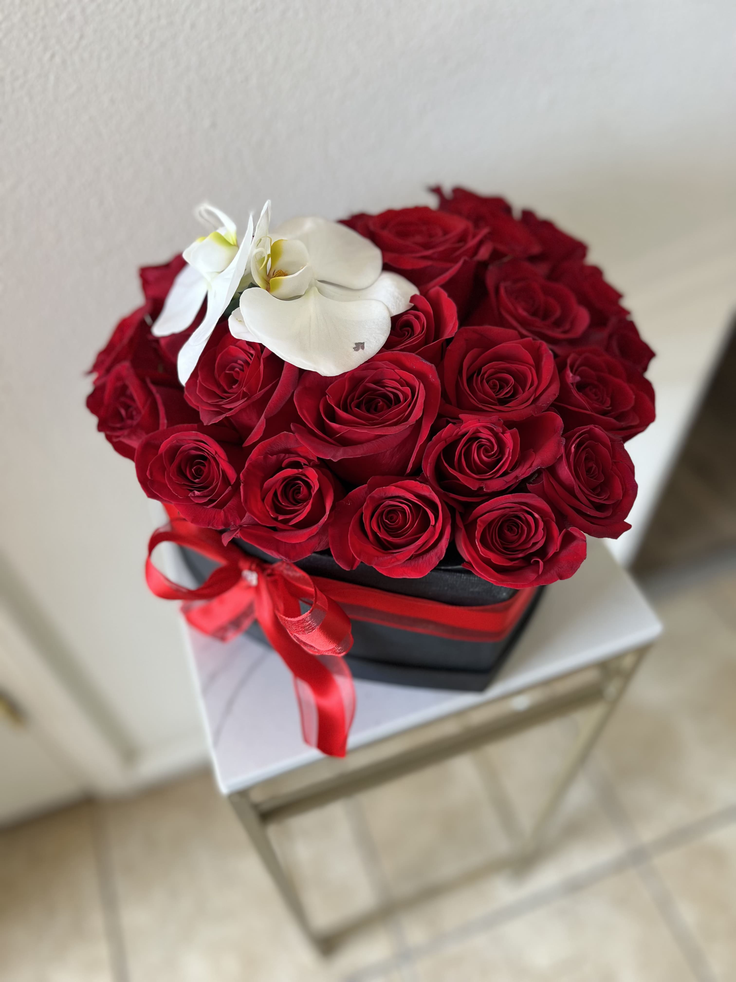 The Orchid Kiss Box The Orchid Kiss Box - Fall in love at first sight with The Orchid Kiss Box — a luxurious floral arrangement handcrafted to perfection for your most cherished moments. Nestled in a sleek, black heart-shaped box, this romantic gift showcases premium red roses arranged in a lush, symmetrical bloom, crowned by two pristine white orchids, the timeless symbol of elegance and rare beauty. Perfect for anniversaries, Valentine’s Day, wedding proposals, or simply to say “I love you” in the most unforgettable way.