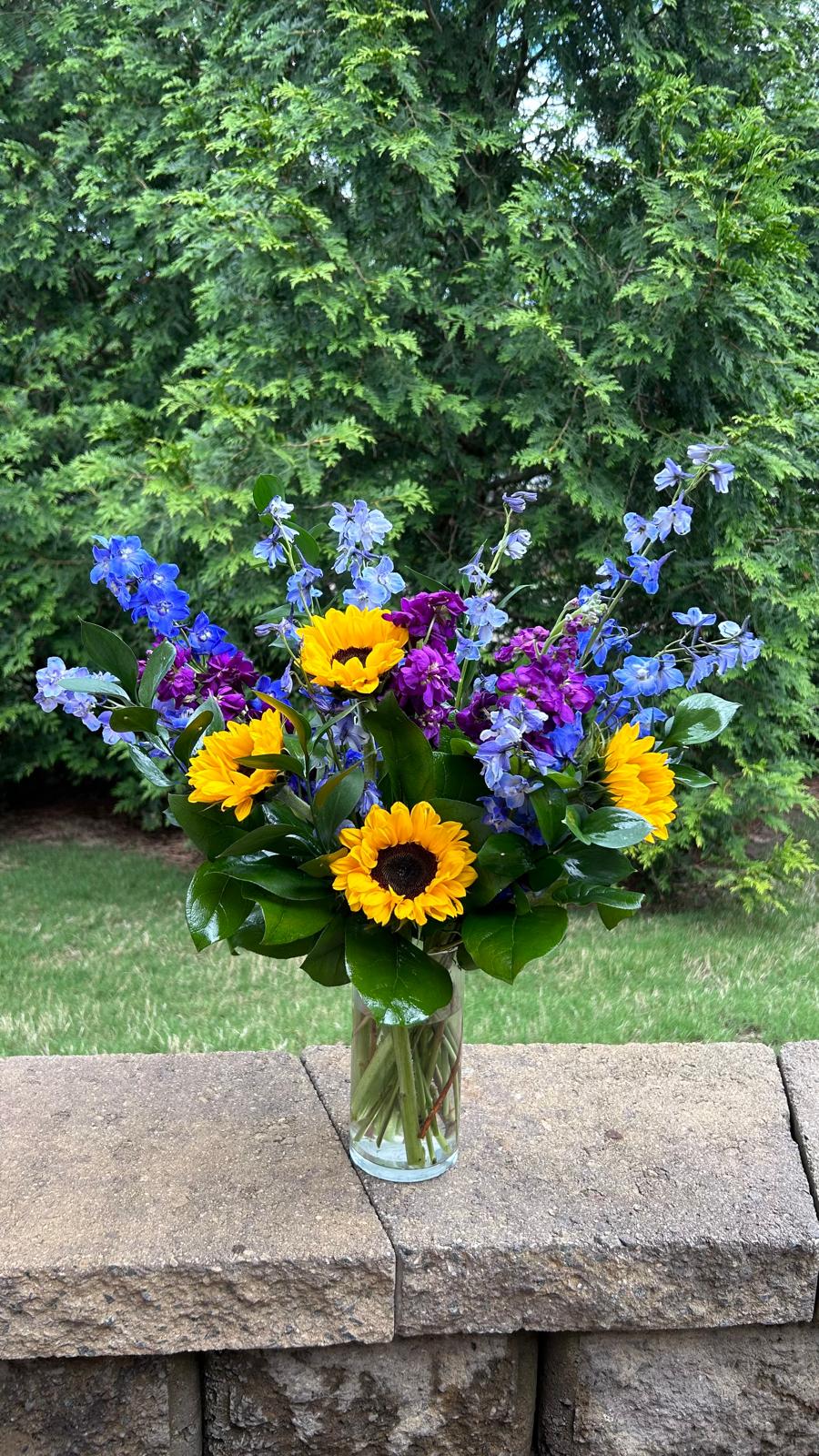 Alexa  - Travel to a warm summer day with the Alexa Bouquet, a glorious blend of yellow, blue, and purple florals. Clear Vase All Occassion  Place your Order Online Monday to Saturday before 1:00 p.m. (E.T.) for same-day delivery. “Orders received after hours will be delivered the next business day”. Check our coverage area.  Occasionally, flowers and/or container substitutions happen due to weather, seasonality, and market conditions, which may affect availability. If this is the case with the gift you’ve selected, we will ensure that the style, theme, and color scheme of your arrangement are preserved and will only substitute items of equal value or higher value.  CARE INSTRUCTIONS Keep the flower arrangement hydrated with natural water and change the water every two days. Do not spray any cleaning product on the flower arrangement. Do not place heavy objects directly on the flower arrangement. Keep flower arrangements out of direct sunlight and extreme heat.