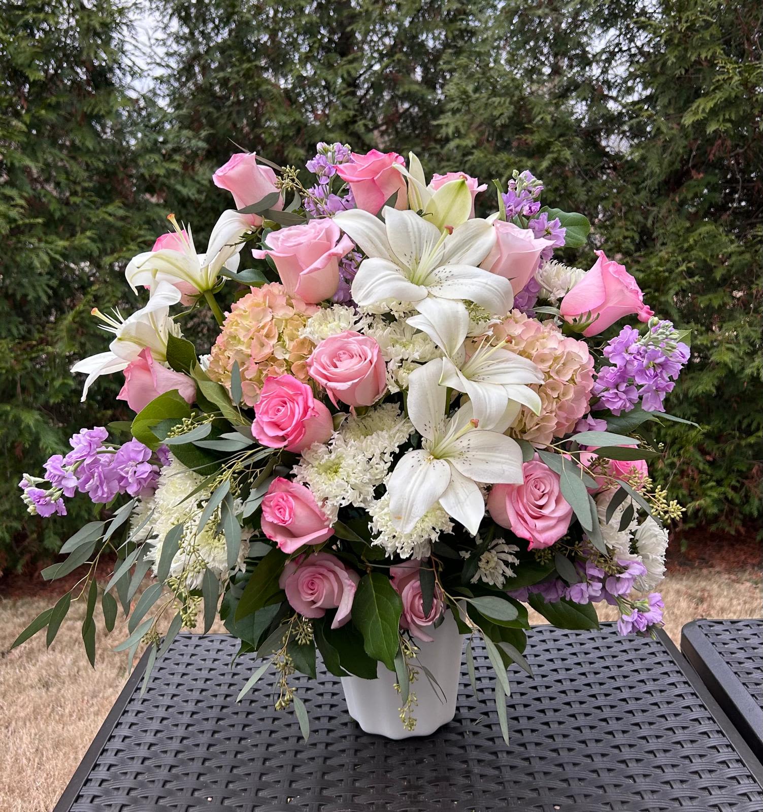 Ara  - Flowers Deluxe along fine foliage. Versatile White Plastic Container  Place your Order Online Monday to Saturday before 1:00 p.m. (E.T.) for same-day delivery. “Orders received after hours will be delivered the next business day”. Check our coverage area. Occasionally, flowers and/or containers are substituted due to weather, seasonality, and market conditions, which may affect availability. If this is the case with the gift you’ve selected, we will ensure that your arrangement's style, theme, and color scheme are preserved and will only substitute items of equal value or higher value.  CARE INSTRUCTIONS Keep the flower arrangement hydrated with natural water and change the water every two days. Do not spray any cleaning product on the flower arrangement. Do not place heavy objects directly on the flower arrangement. Keep flower arrangements out of direct sunlight and extreme heat.