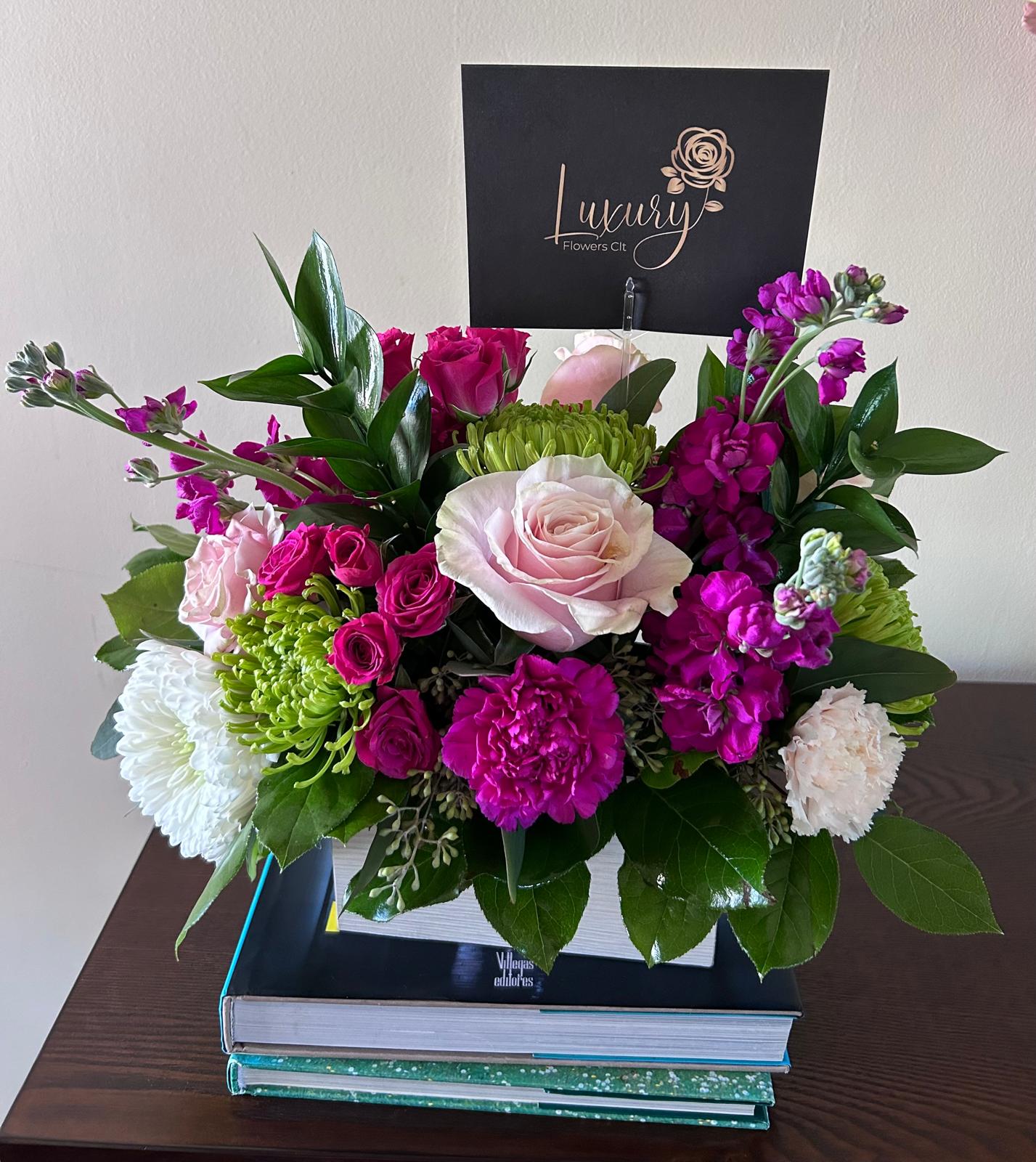 Beca Wooden Box - Fresh flower arrangement along fine foliage. Bloom Details: Roses, Fancy Carnation, White Mums, Spray Roses, Purple Stock WHITEWASHED WOODEN BOX  All Occasion  Place your Order Online Monday to Saturday before 1:00 p.m. (E.T.) for same-day delivery. “Orders received after hours will be delivered the next business day”. Check our coverage area.  Occasionally, flowers and/or container substitutions happen due to weather, seasonality, and market conditions, which may affect availability. If this is the case with the gift you’ve selected, we will ensure that your arrangement's style, theme, and color scheme are preserved and will only substitute items of equal value or higher value.  CARE INSTRUCTIONS Gently mist the arrangement with natural water every other day. Do not spray any cleaning product on the flower arrangement. Do not place heavy objects directly on the flower arrangement. Keep them out of direct sunlight and extreme heat. 