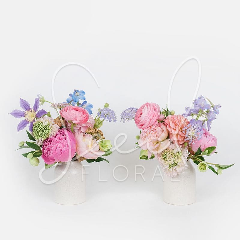 Petite Bloom Duo - A charming set of two mini arrangements bursting with seasonal blooms in cheerful shades of pink, lavender, blush, and soft blue. Perfectly paired in sleek white ceramic vases, this whimsical set adds a touch of joy and color to any space—ideal for gifting or brightening up your desk, nightstand, or dining table.