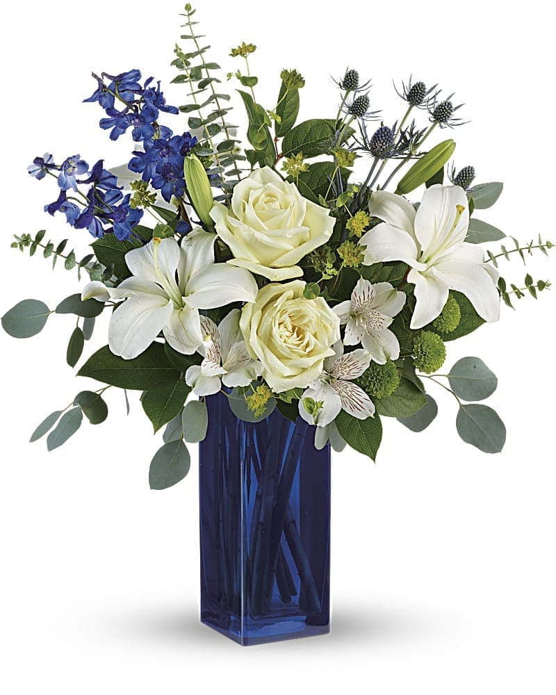 Teleflora's Calming Cobalt Bouquet - A classic for any occasion, this timeless bouquet of white roses and fragrant lilies in a rich, cobalt glass vase is sure to impress and delight. This arrangement includes white roses, white asiatic lilies, white alstroemeria, green button spray chrysanthemums, blue eryngium, bupleurum, spiral eucalyptus, silver dollar eucalyptus, and lemon leaf. Delivered in a Blue Bunch vase.