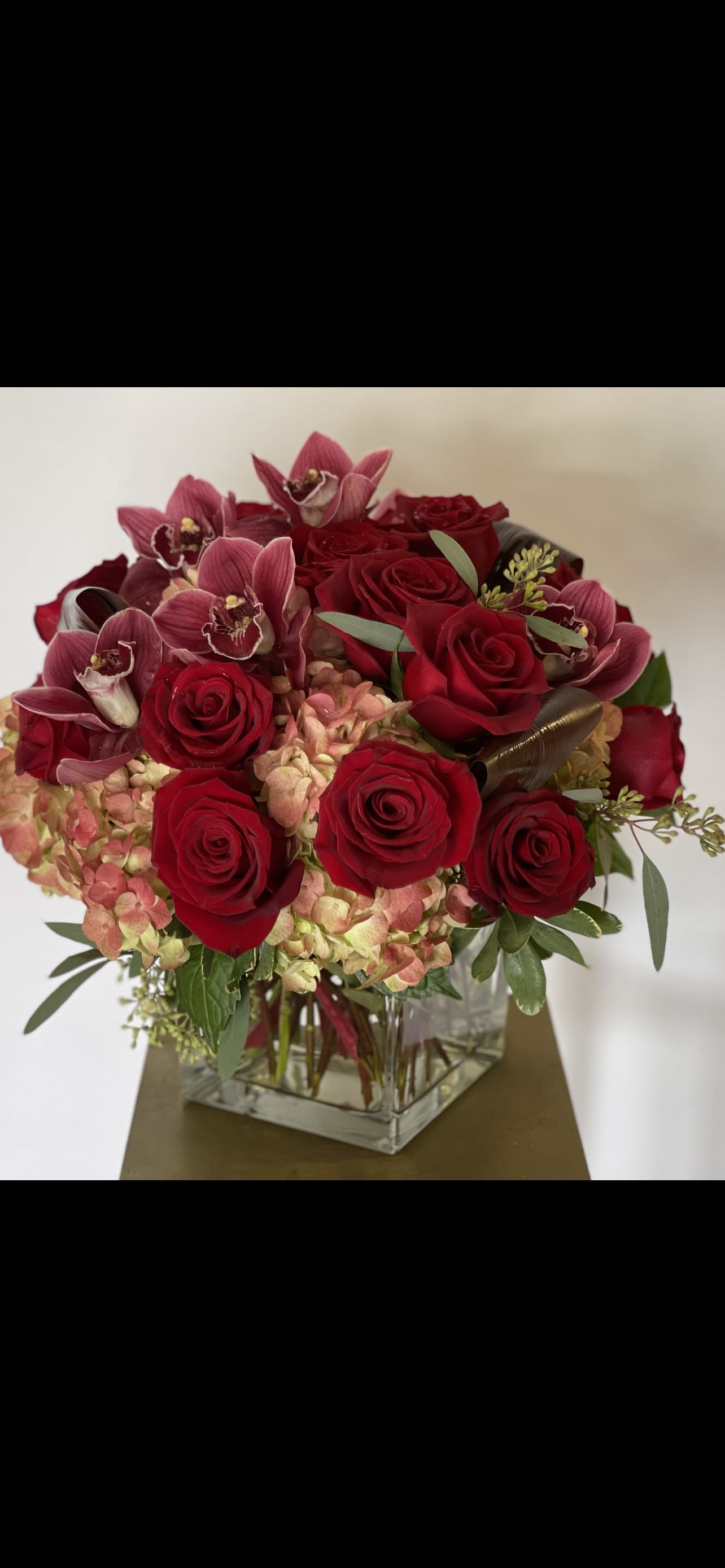 Crimson Love Crimson Love - Orchids, roses and hydrangea! This mix is perfection, red roses, burgundy cymbidium orchids and hydrangea in a large glass cube
