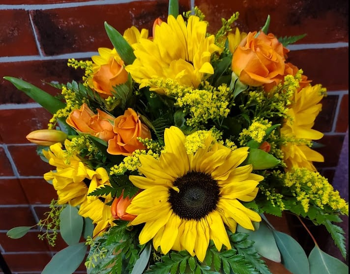 Orange and Yellow - A beautiful all around arrangement designed with fresh flowers to include Sunflowers, spray roses and solidago.  * Some stages of flower life may vary. (Example: Lilies may be more open than imaged.)  Flower shortages and product availability means that some substitutions will apply. Value will always be filled. This bouquet might include eucalyptus amongst the greenery. It may be toxic to pets including but not limited to Cats and Dogs if digested.