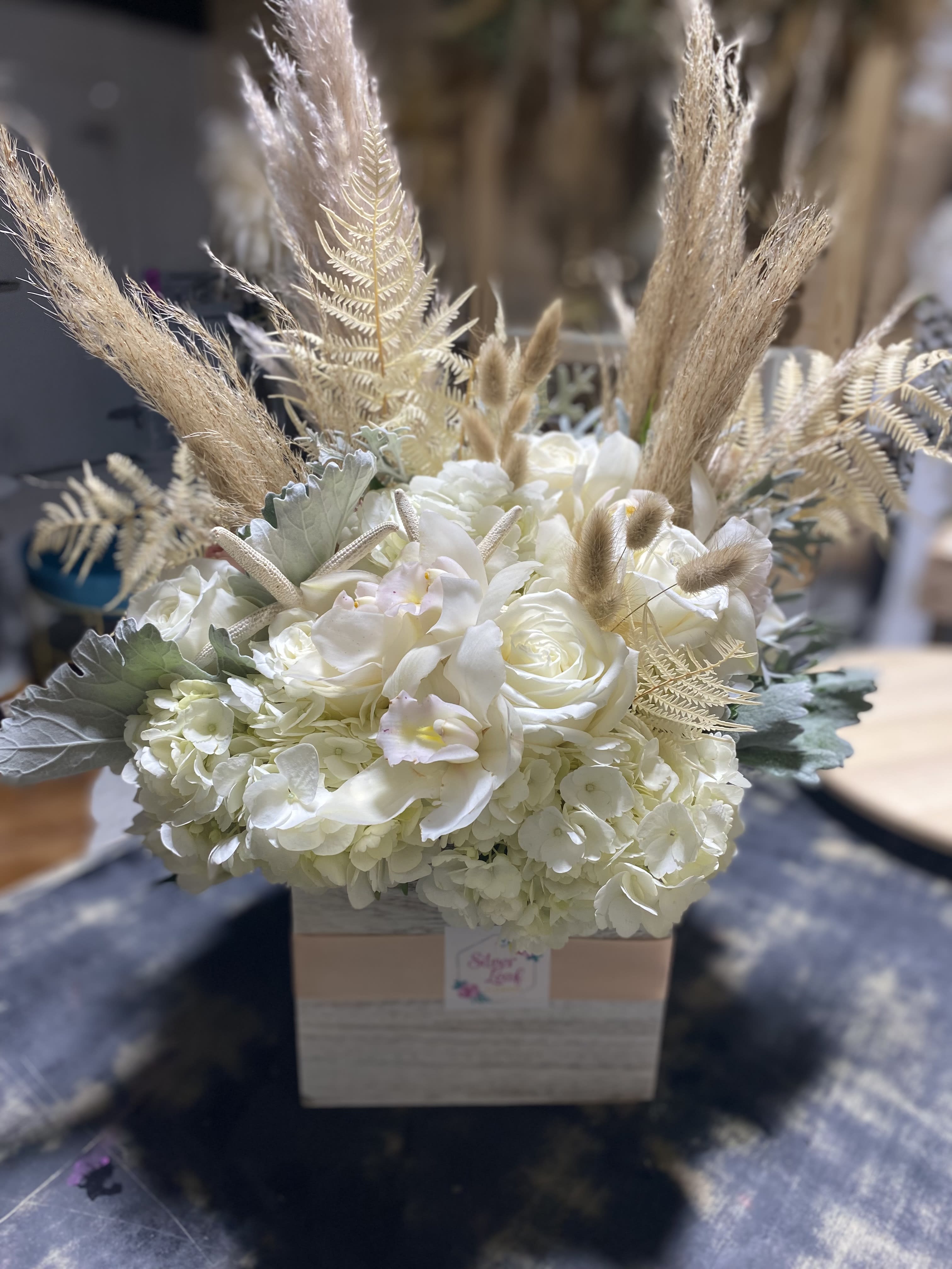 White Sea Shell FL - A large white wood box fill with premium blooms with accent of Florida vibe with sea shells and some orchids blooms   Approximate Dimensions: 13&quot;D x 18&quot;H