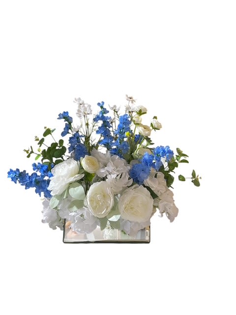 Ledge Floral - Description: Silk floral  &quot;Enchanted Seascape Blooms is a captivating floral arrangement that brings the beauty of spring to life in a rectangular container. The arrangement features of open blooms and roses in pastel hues, creating a soft and elegant look. Nestled among the blooms are whimsical wild dolphins crafted from delicate materials, adding a touch of magic and playfulness to the display. Shimmering pennies scattered throughout the arrangement provide a hint of sparkle and charm, enhancing the overall enchanting effect. This unique and beautiful arrangement is sure to inspire wonder and delight in all who behold it.&quot;  Size showing - Deluxe   22''x25'' 