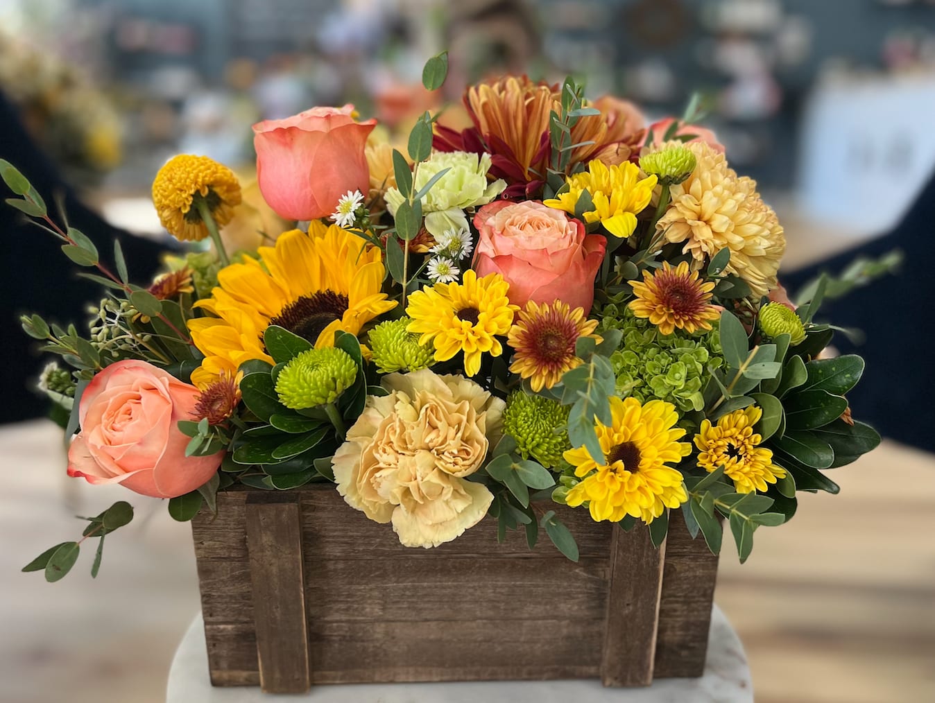 Autumn Box - This beautiful bouquet features a mix of vibrant sunflowers and delicate roses, arranged in a charming wooden box. Perfect as a thoughtful gift or a get well present this arrangement is sure to bring joy and warmth to any occasion. 