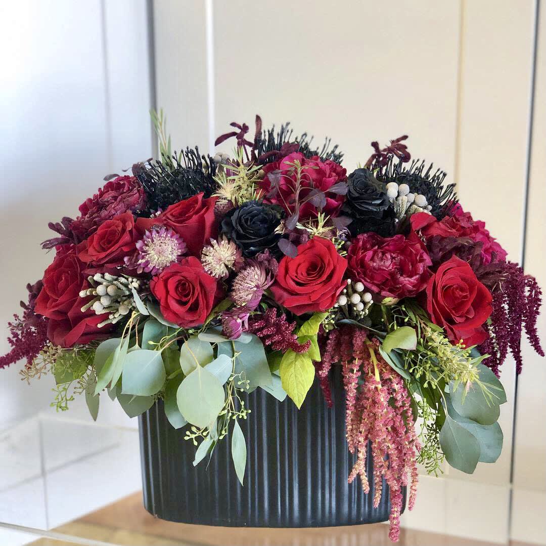 Halloween Delight - Fresh Black Roses, Eucalyptus, Amaranthus, Pincusion Protea and more - A spooky delight of black and red florals in a black ceramic vase. This thrilling arrangement in a showstopper for Halloween and beyond. 