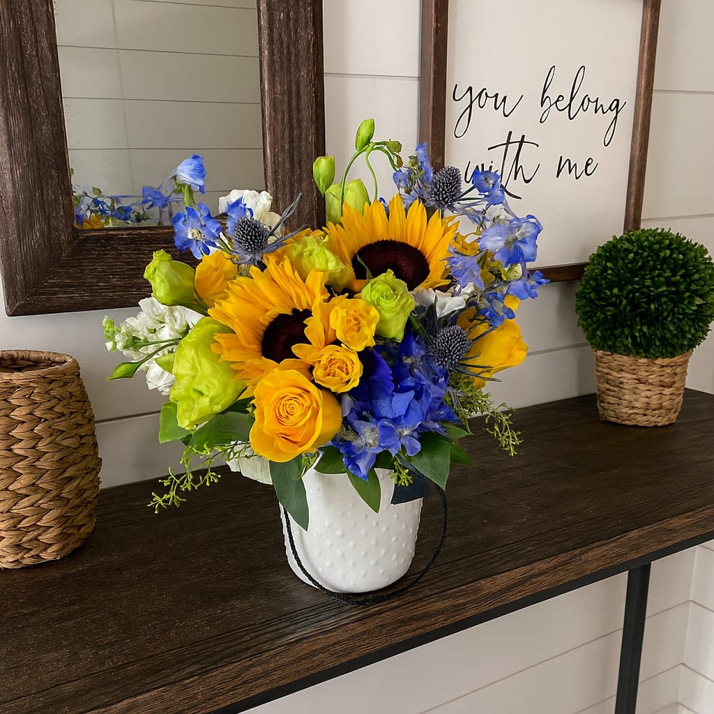 Here Come's The Sun - Here Comes the Sun – Bright and Cheerful Floral Arrangement  Bring warmth and happiness into any space with Here Comes the Sun, a radiant flower arrangement inspired by the iconic Beatles song. Designed in a rustic vase, this cheerful bouquet showcases a stunning mix of sunflowers, yellow roses, hydrangeas, lisianthus, thistle, and blue delphinium. The vibrant blend of sunny yellows and bright blues creates the perfect balance of joy and elegance, making it ideal for summer celebrations, housewarmings, or simply as a “just because” gift.  Much like the song that inspired it, Here Comes the Sun embodies hope, renewal, and timeless beauty—a floral arrangement guaranteed to brighten anyone’s day and bring a touch of sunshine indoors.