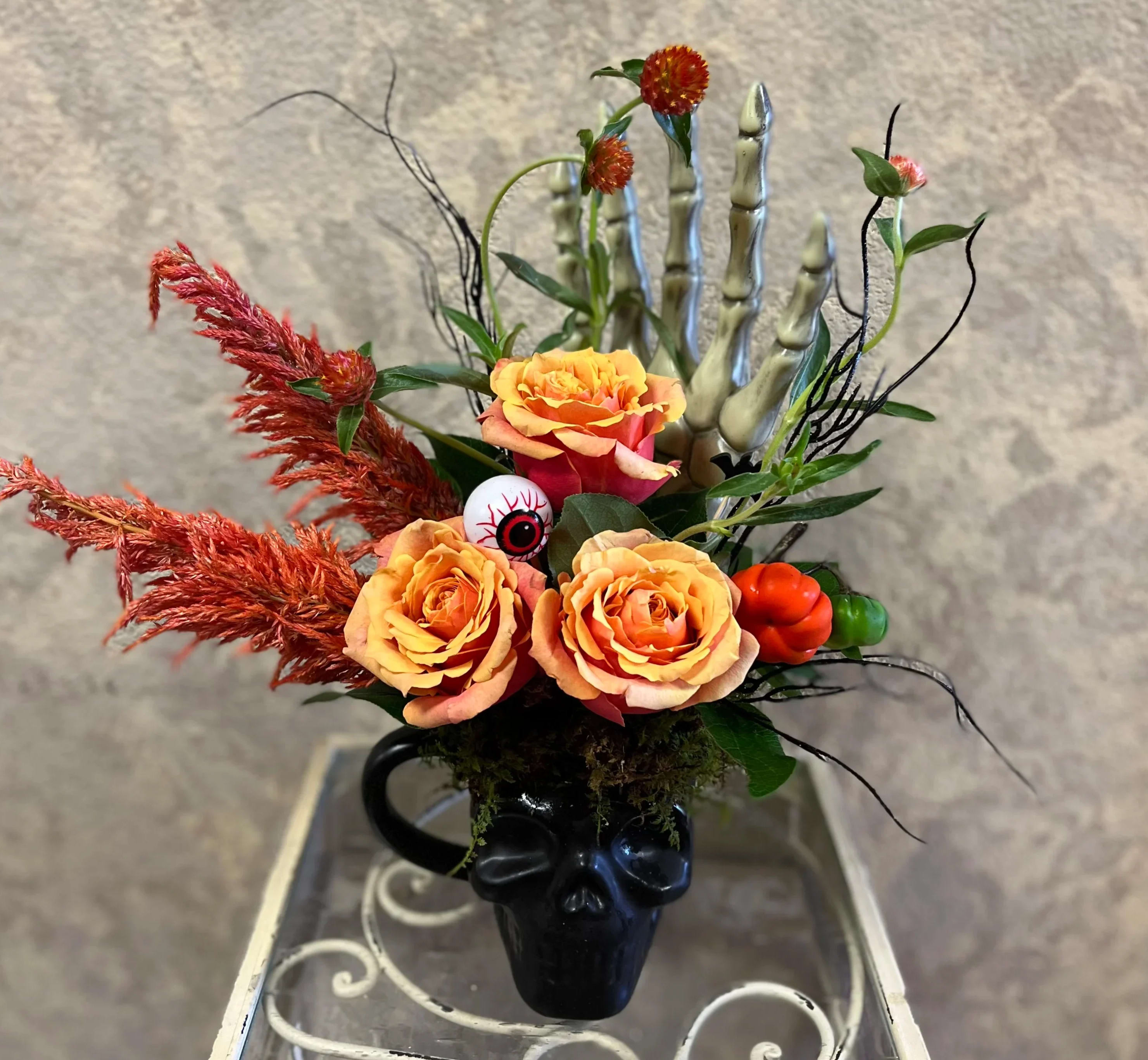 Sweet but Spooky - Type of Flowers: Orange Roses, Amaranthus, Branches, and moss with halloween accents in a skull mug. Availability: October only, SKULL MUGS MAY VARY DEPENDING ON AVAILABILITY Design View: Symmetric Front Facing View Photo shown: Standard