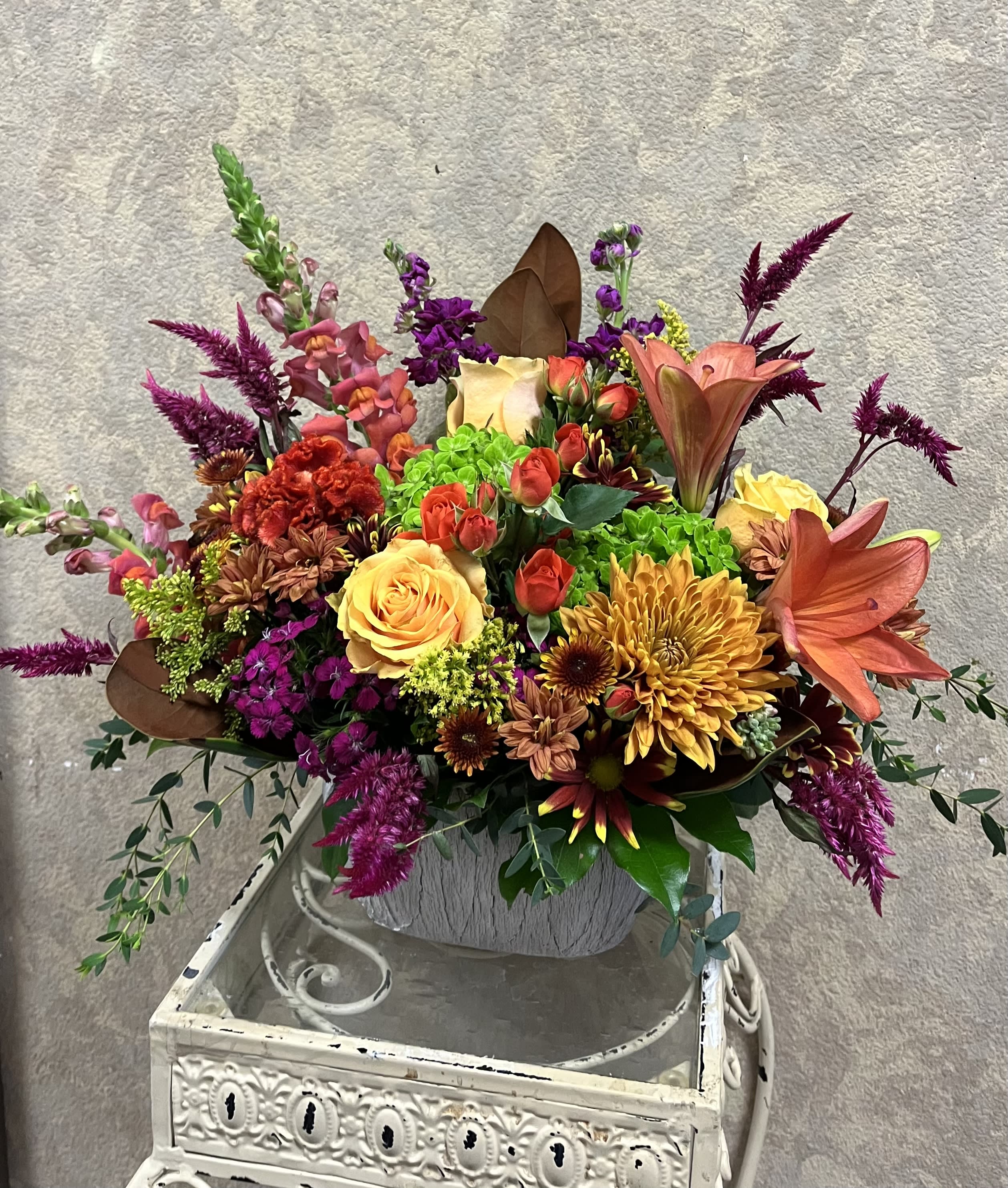 Stay Humble Stay Humble - Recipe: Brown Chrysanthemums, Orange Roses, Spray Roses, Blood Orange Lilies, Snapdragons, Protea, Green Hydrangeas, Fuchsia Amaranthus, Stock, Daisies, Eucalyptus and Magnolia Leaves in a white oval, ceramic vase. Availability: All year round Design View: Symmetric Front Facing View Photo shown: Standard