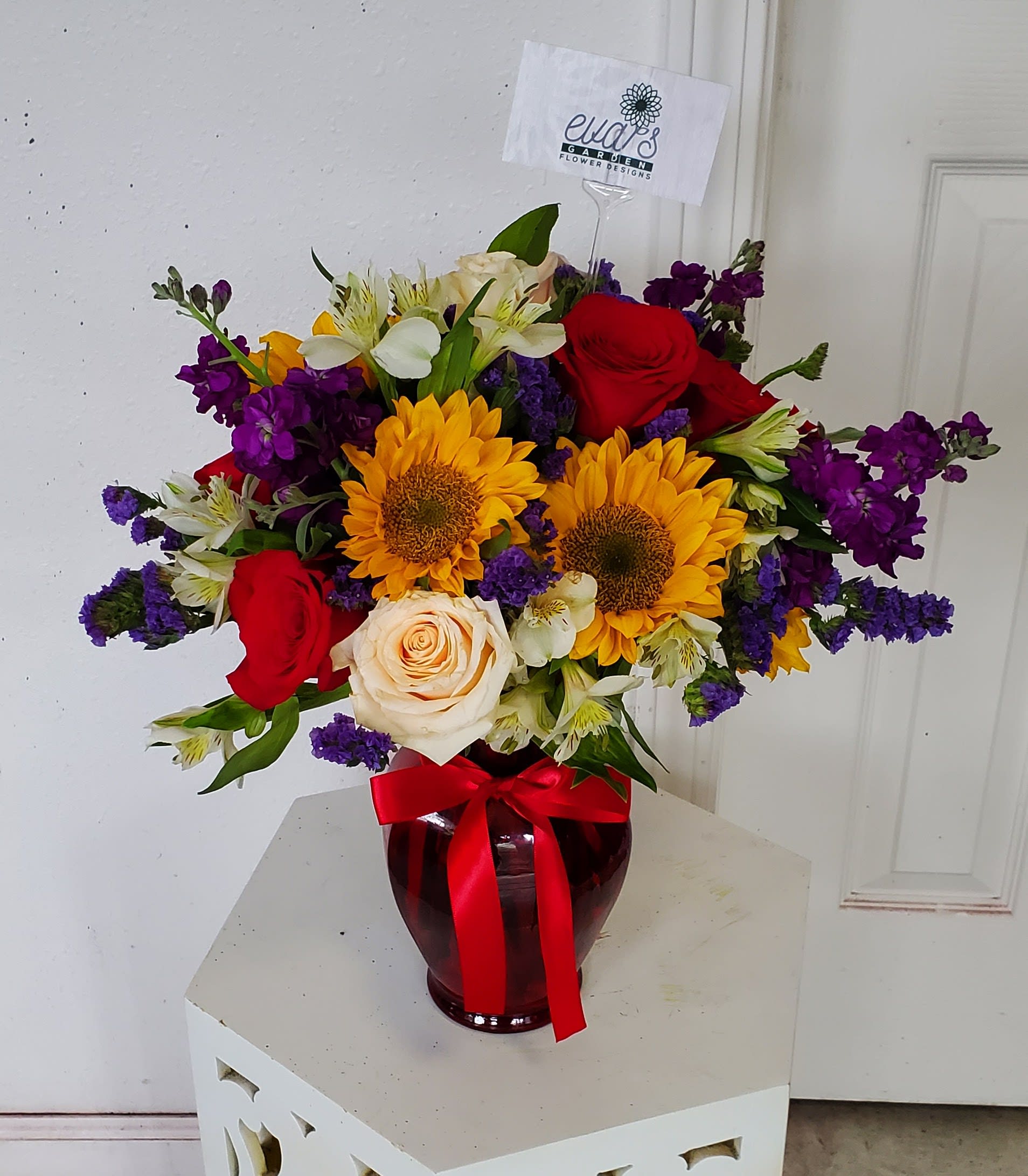 Brilliant Arrangement - Crystal red vase with sunflowers, alstroemeria, stock, roses, and statice.   (Picture depicts premium; ONLY PREMIUM IS AVAILABLE FOR THIS ARRANGEMENT)