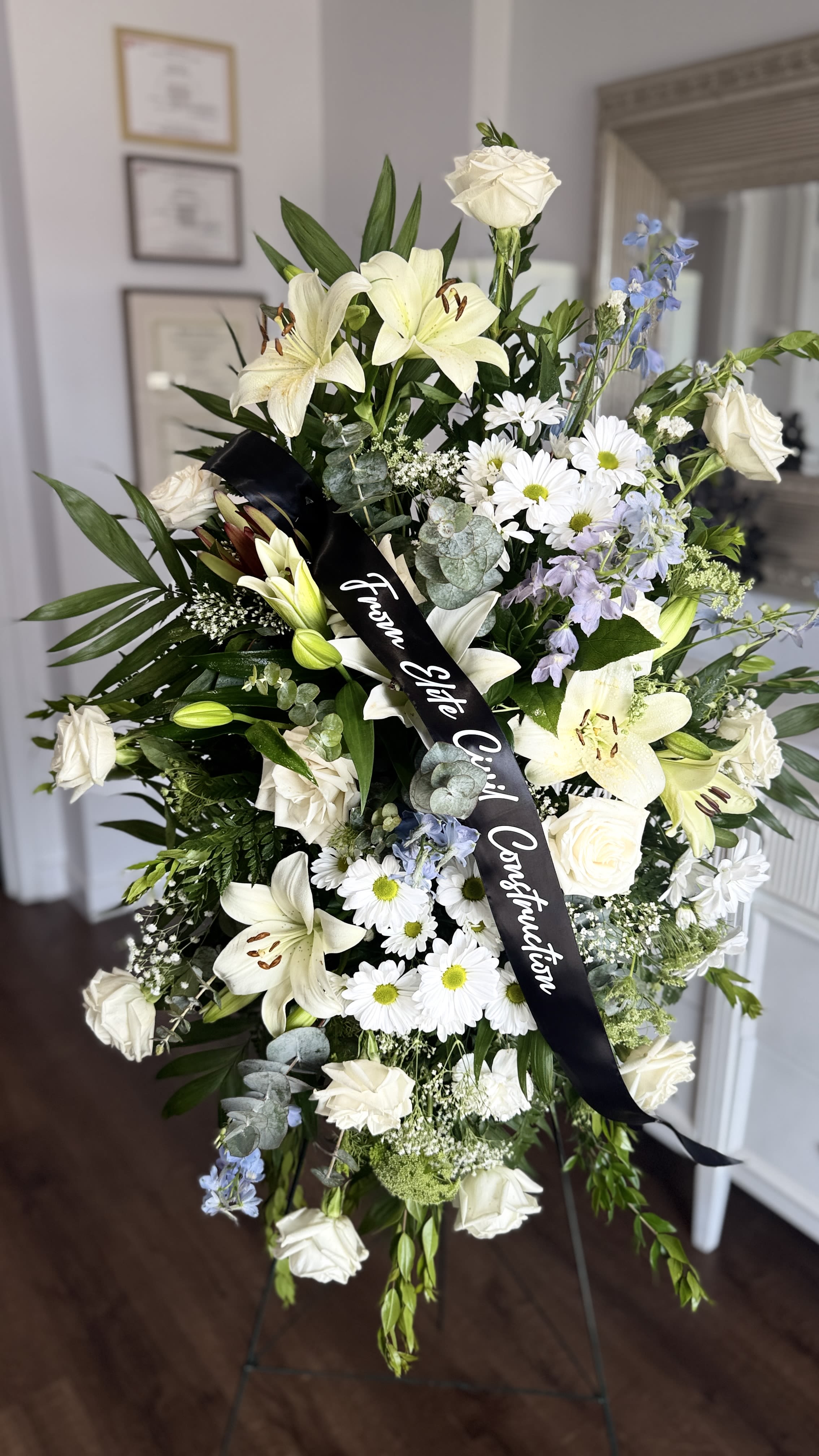 With Deepest Sympathy spray  - A traditional sympathy standing spray beautifully arranged with an array of White Payablanca Roses, Casablanca lilies, Daisies and a touch of blue delphinium to symbolize calm &amp; peace. Also included is a great variety of greens from eucalyptus leaves, emerald ferns and, leather leafs to give it a natural look to the arrangment Sache is included with purchase and is customizable to your unique message you want to convey (please add sache info under card or message info)