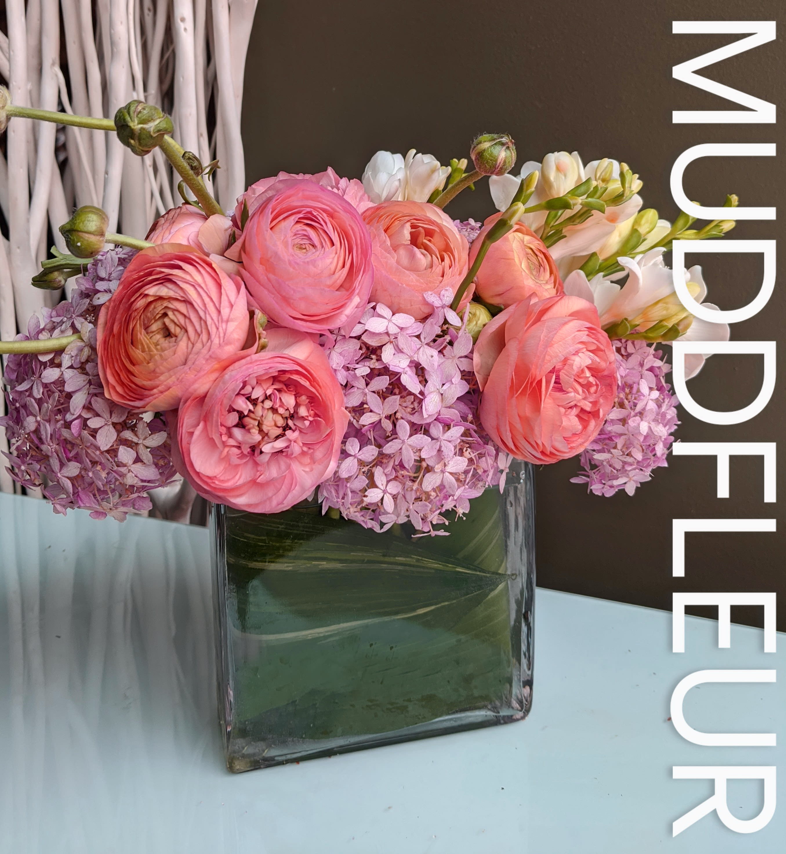 Ranunculus Lovers  - This petit vase features a garden favorite, the delicate ranunculus.  Shown here in gorgeous peach with pink hydrangea in petit rectangle vase with ti leaf accent.  Shown here with white freesia, but colors and combination of flowers varies based on availability. 