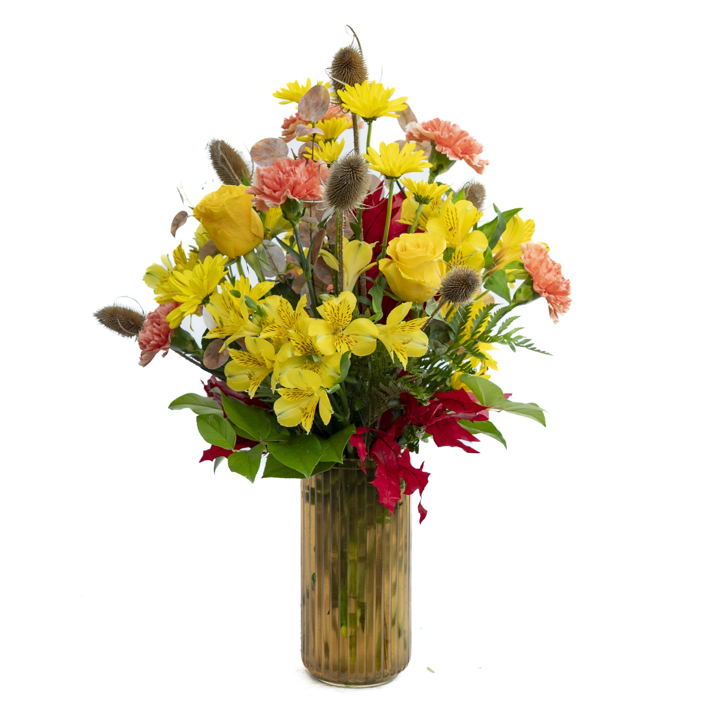 Golden Autumn Bouquet - Approximately 24 1/2&quot; x 16&quot;   Bright and cheerful, this vibrant arrangement features sunny yellow roses, alstroemeria, and daisies paired with orange carnations and accented by rustic thistle pods and lush greenery. Hints of deep red foliage add a touch of autumn warmth, all beautifully displayed in a tall amber glass vase. Perfect for celebrating the season or bringing a burst of sunshine indoors.