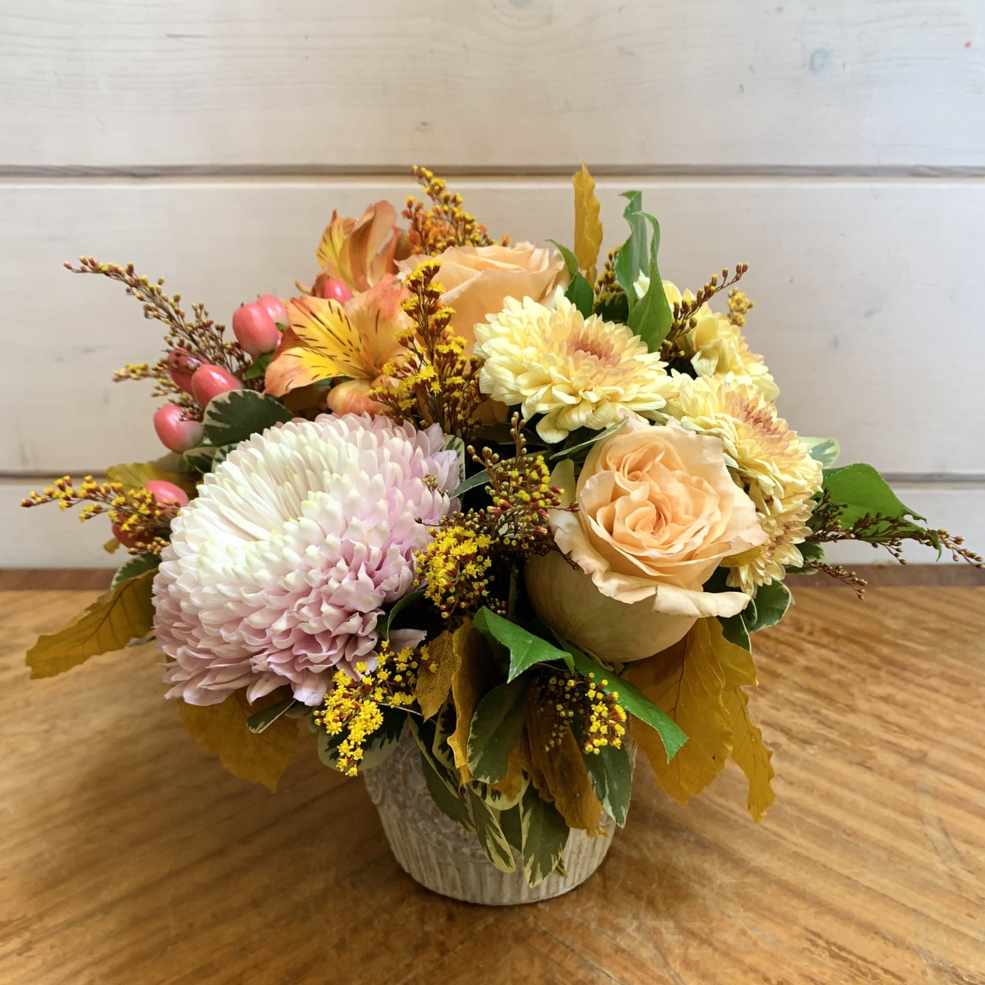 Fall Beauty - Shimmer roses, soft peach and yellow crysanthemums, hypericum berries, and orange alstroemeria arranged in a molded grey pot with seasonal filler flowers and fall foliage. Approximately 12&quot; tall and 9&quot; wide.