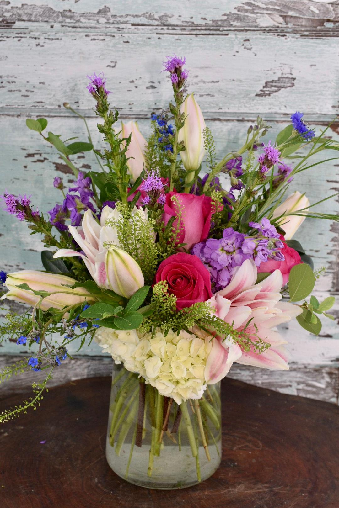 Make Plans - Bright pink roses and stargazer lilies come together with purple stock and greenery for this impressive arrangement.   