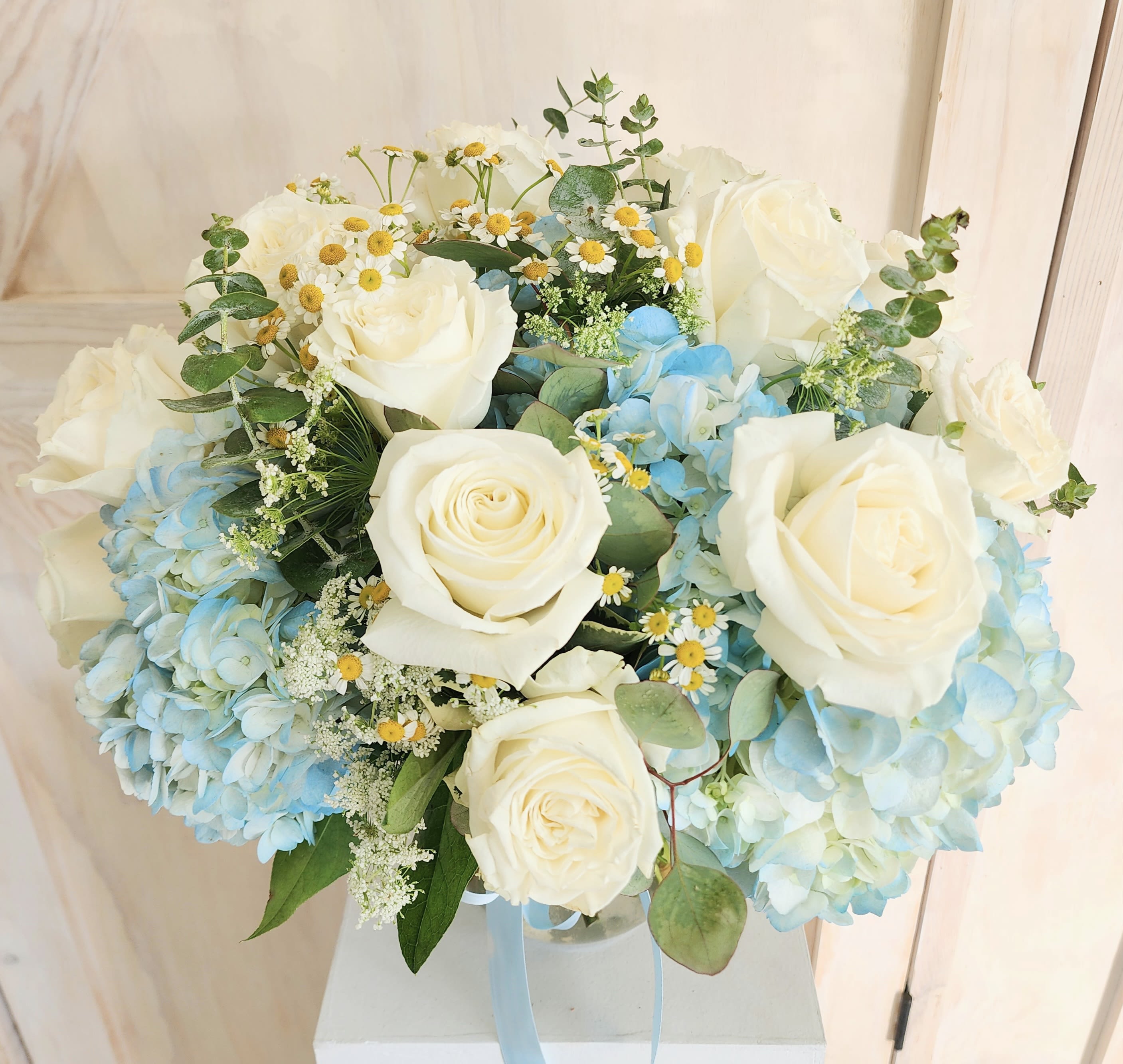 Blue Breeze Bouquet Blue Breeze Bouquet - Several white roses in a square vase either blue hydrangea, chamomile or other filler and eucalyptus.