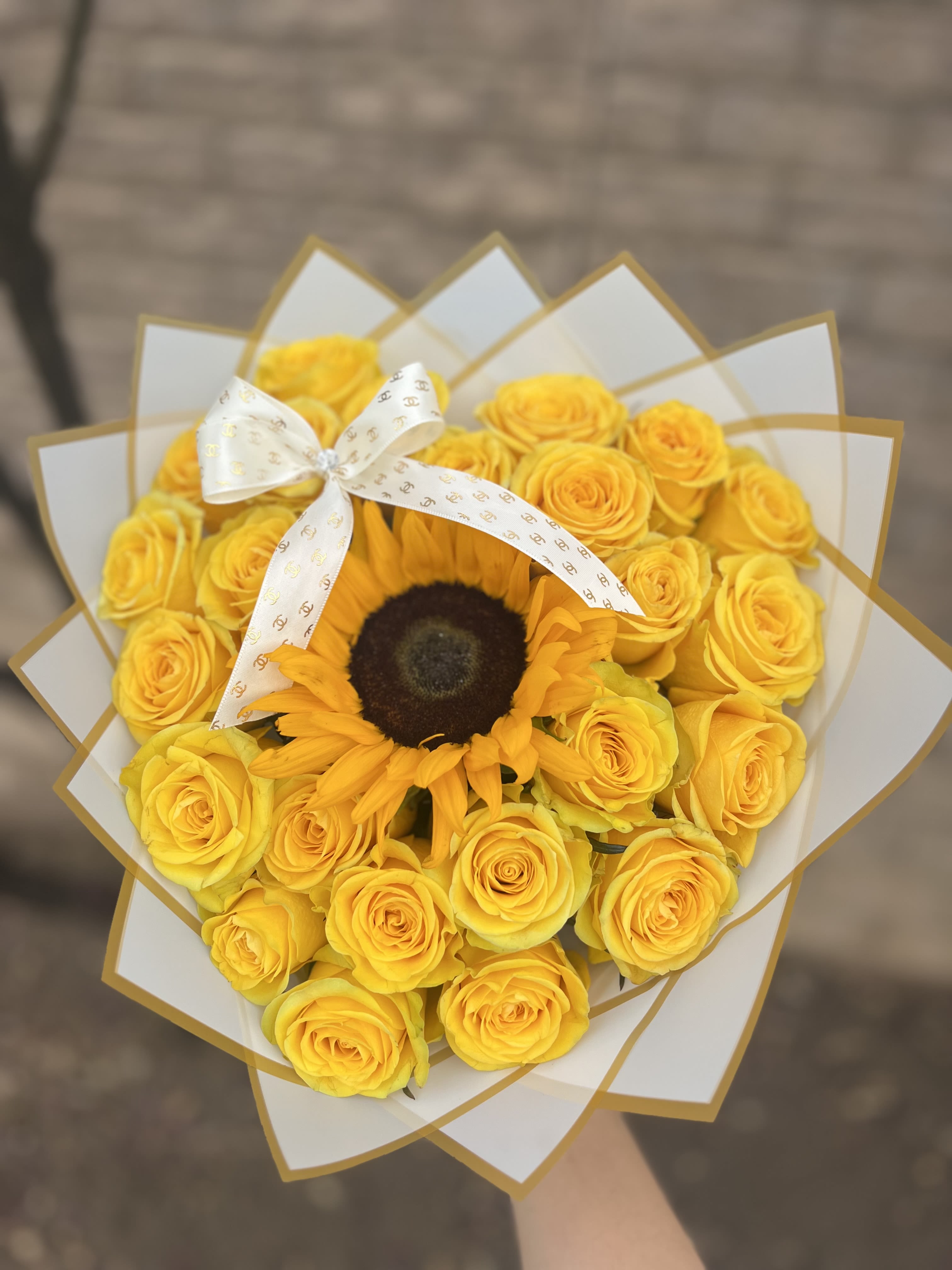 Coquette Sunshine -  A playful yet elegant bouquet that radiates charm and warmth. Golden yellow roses encircle a striking sunflower at the heart, tied together with a delicate ribbon. Perfectly coquettish, it balances bold beauty with a hint of flirtatious sweetness — a bouquet that smiles as brightly as the sun itself.