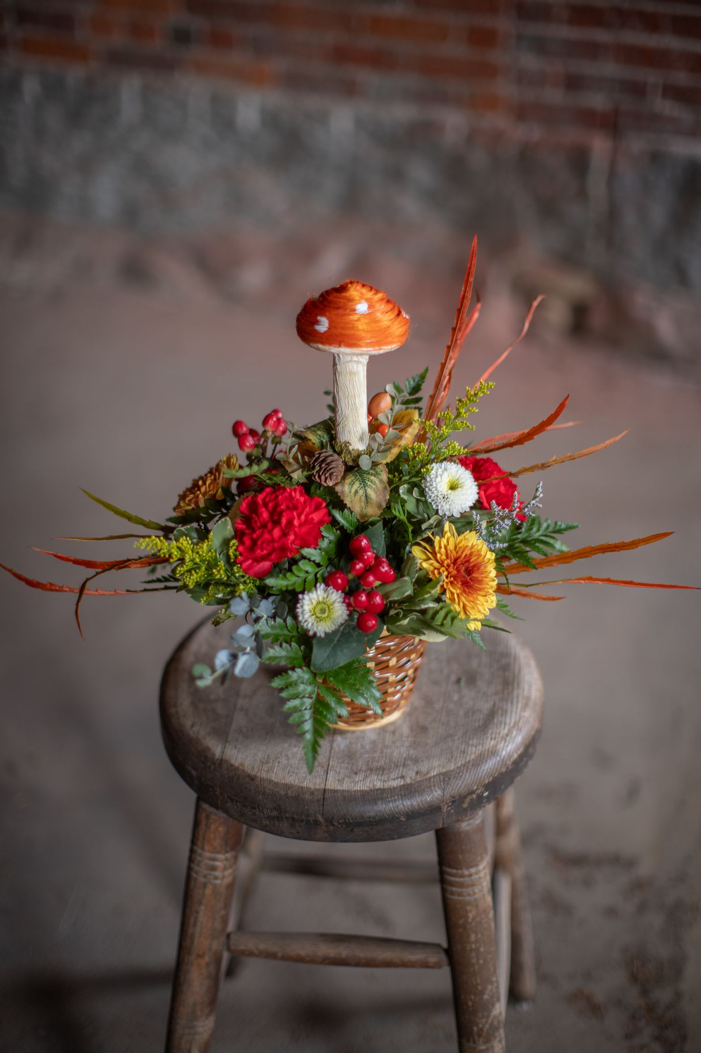 Fungi basket - This fun-guy basket is sure to be a conversation piece. Mushrooms are so one trend and a sign of fall. These sisal mushroom decorations come in bronzy-orange and ivory-cream color and may vary from photo. Autumn mums, carnations and hypericum berries complete this fun forage themed design in a small basket.