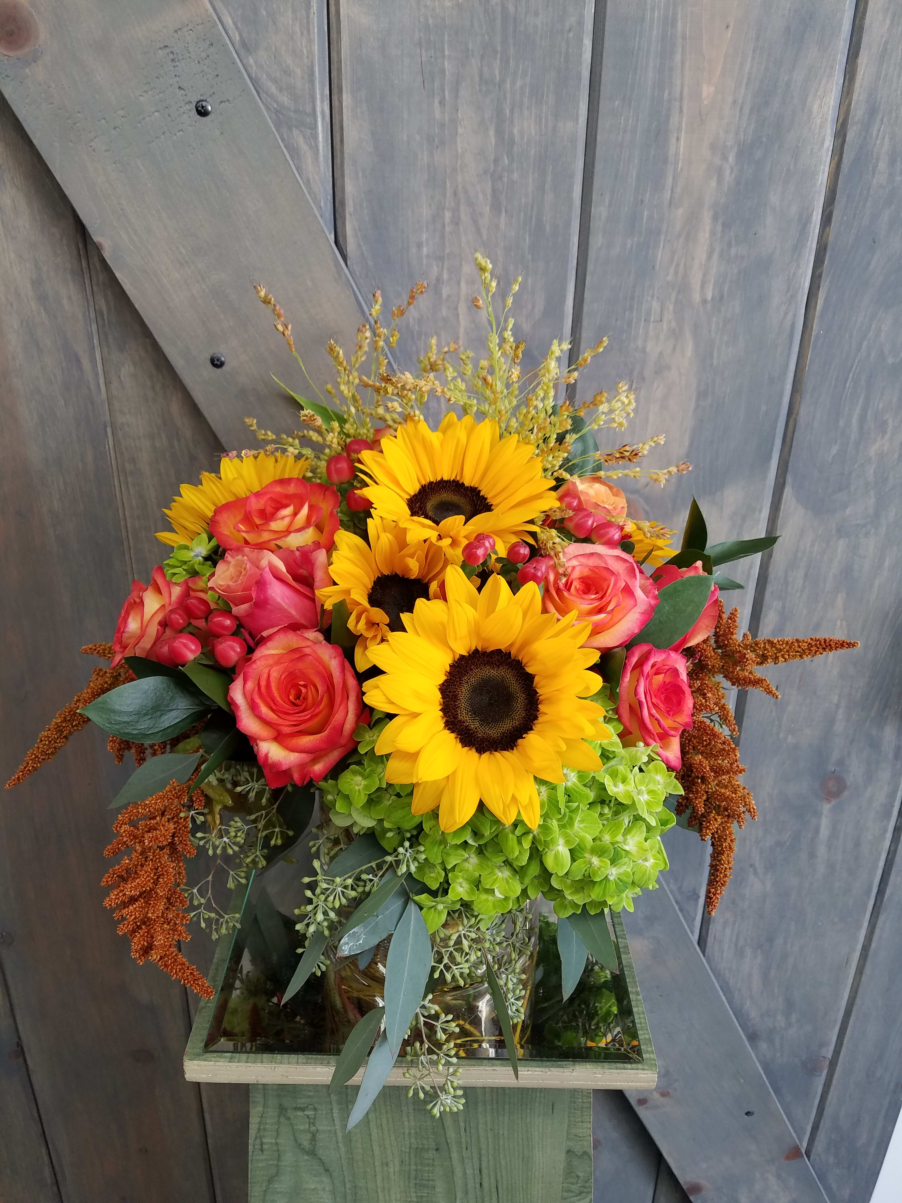 Autumn Embrace - This centerpiece will be a huge hit during this autumn season. Our design include sunflowers, High and Magic Roses, Cherry Brandy Roses, Green hydrangea, Coffee berry, hanging amaranthus, seeded eucalyptus, and millet for the ultimate fall centerpiece