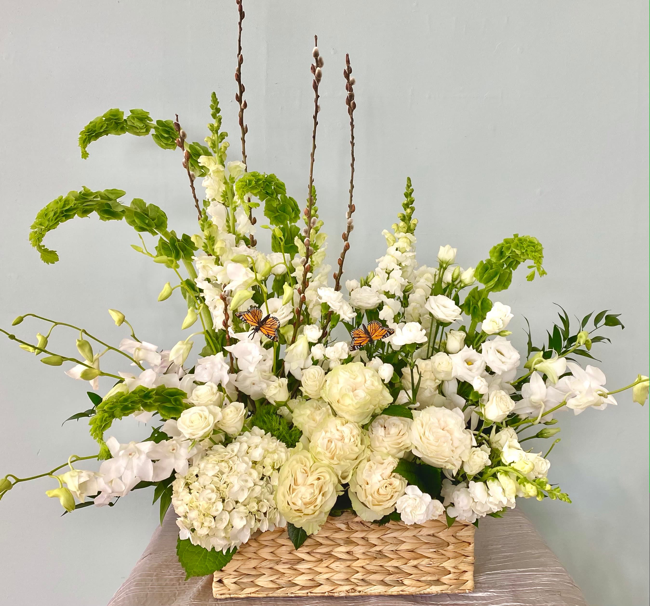 Serenity Garden Basket - A relaxing and heart warming composition of different seasonal white flowers such as orchids, snap dragons, hydrangeas,  etc accented with fresh greens  such as bells of Ireland, dianthus, etc. Butterflies are not part of the design but they can be added on at check out.