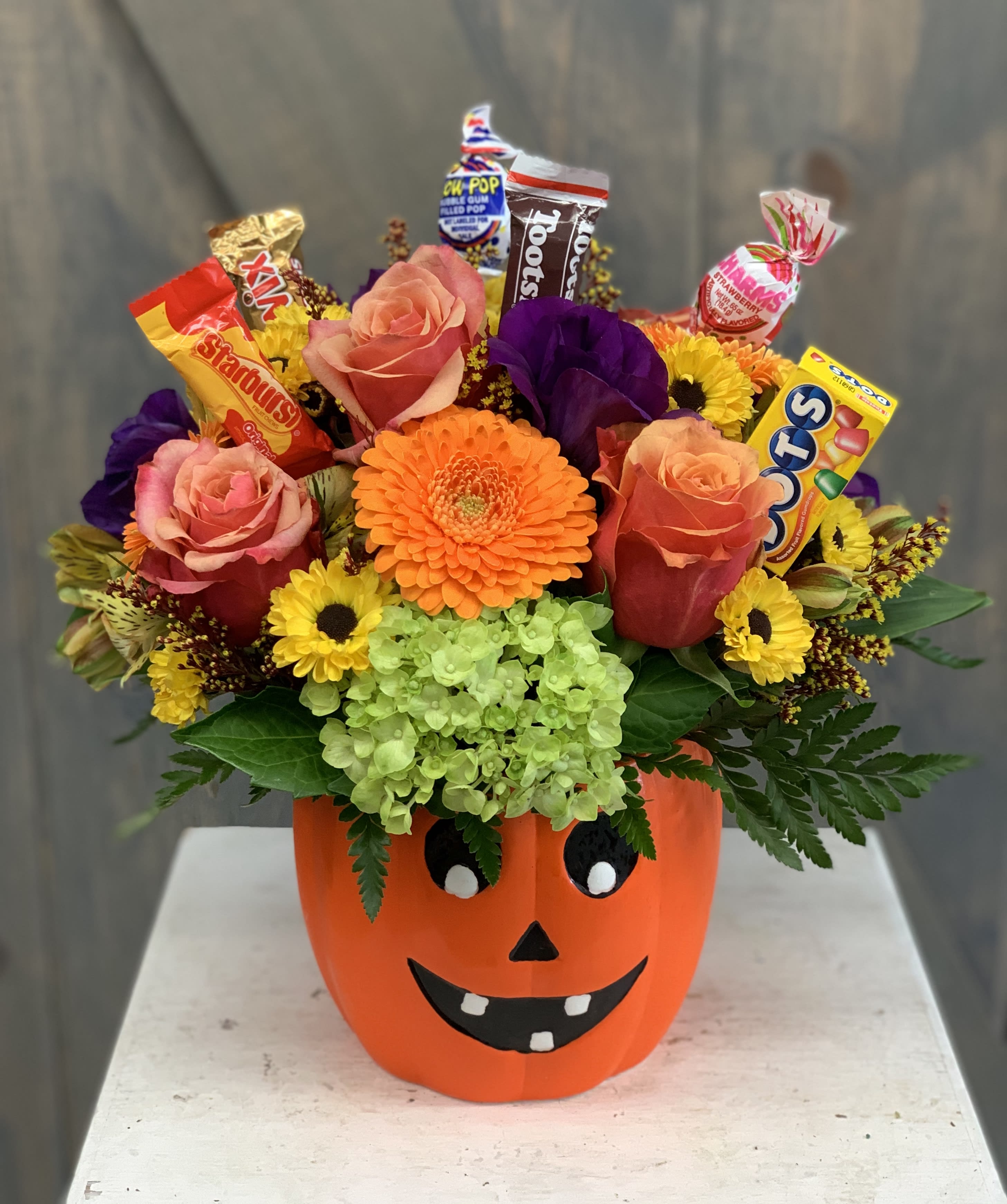 Smiling Jack - A fun and festive Halloween floral arrangement with assorted candy picked inside. Included in this floral design are roses, mums, lisianthius, gerbera daisys, and soldaster all with a ceramic jack o' lantern container