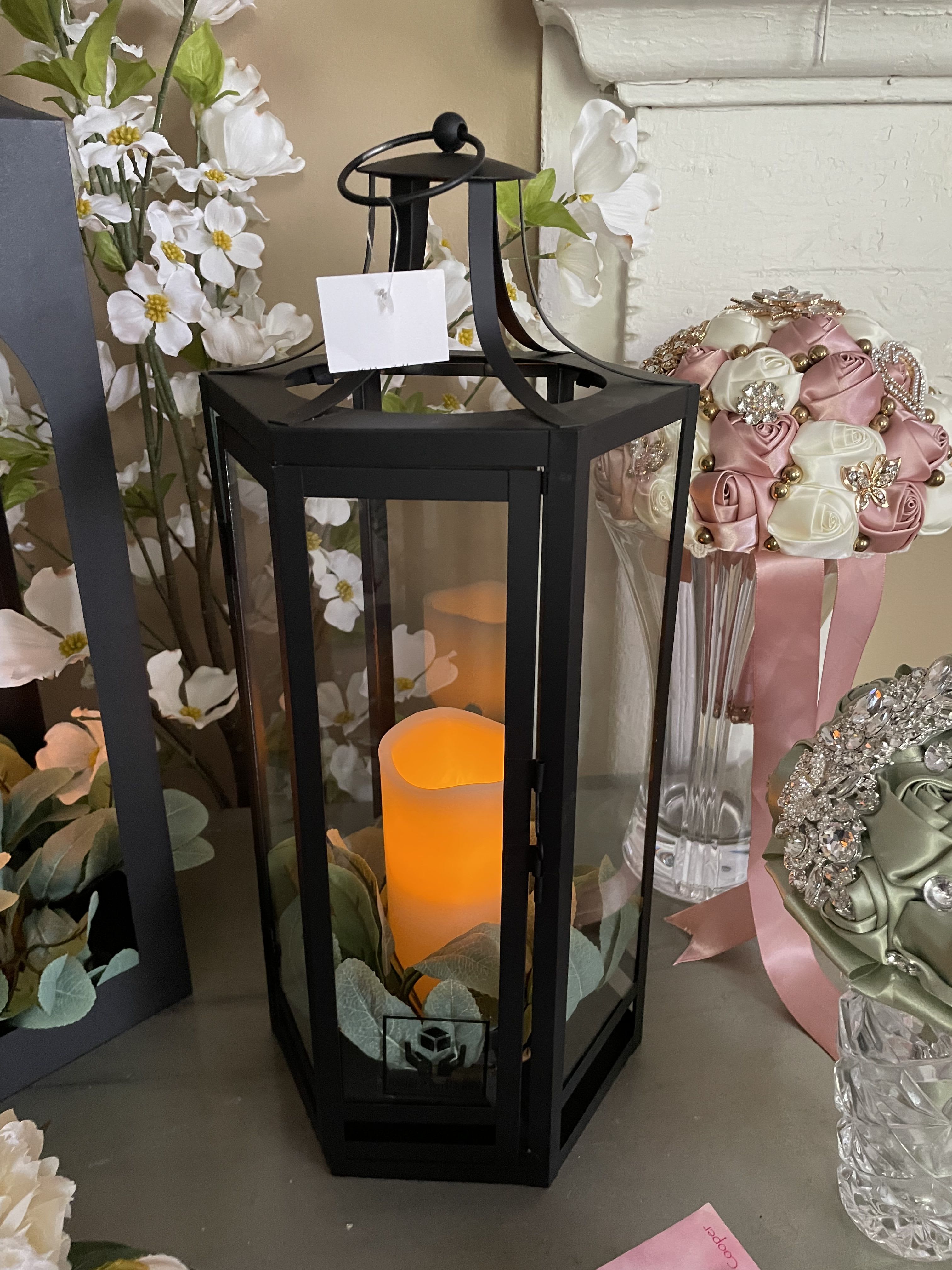 Metal Black Lantern - Their light will always shine in our hearts...A medium sized metal black wood lantern. Glass encased Design. A candle with greenery is placed inside. 