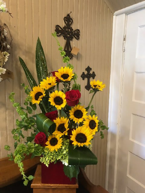 Box of Sunshine - A star is born with this fresh floral mixture of Sunflowers , Red Roses, Wood accents &amp; much more, all nestled into a red bamboo box. One sided, high style arrangement will be the highlight of the room.